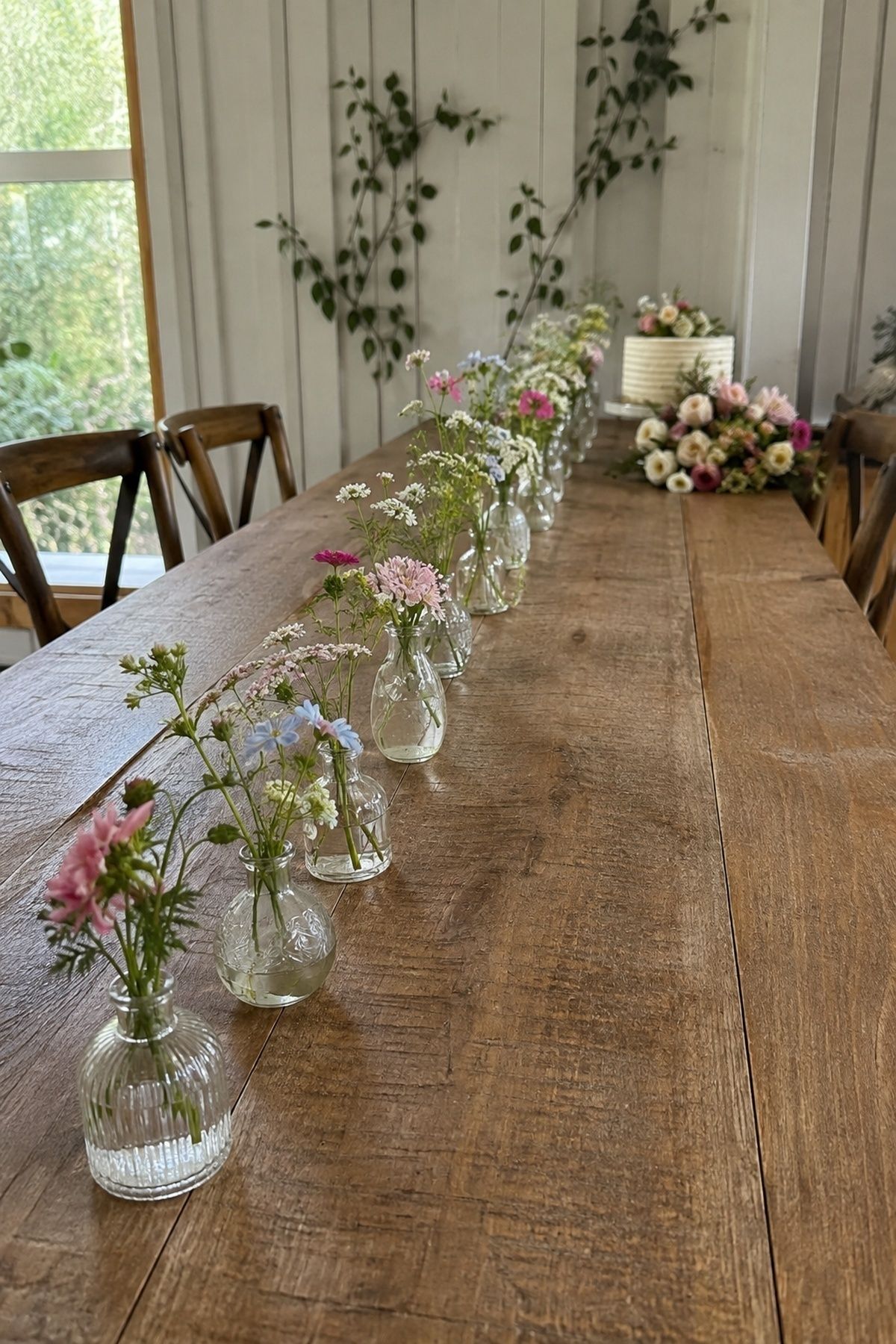 Seasonal wedding flowers arranged in small bud vases along a narrow long table