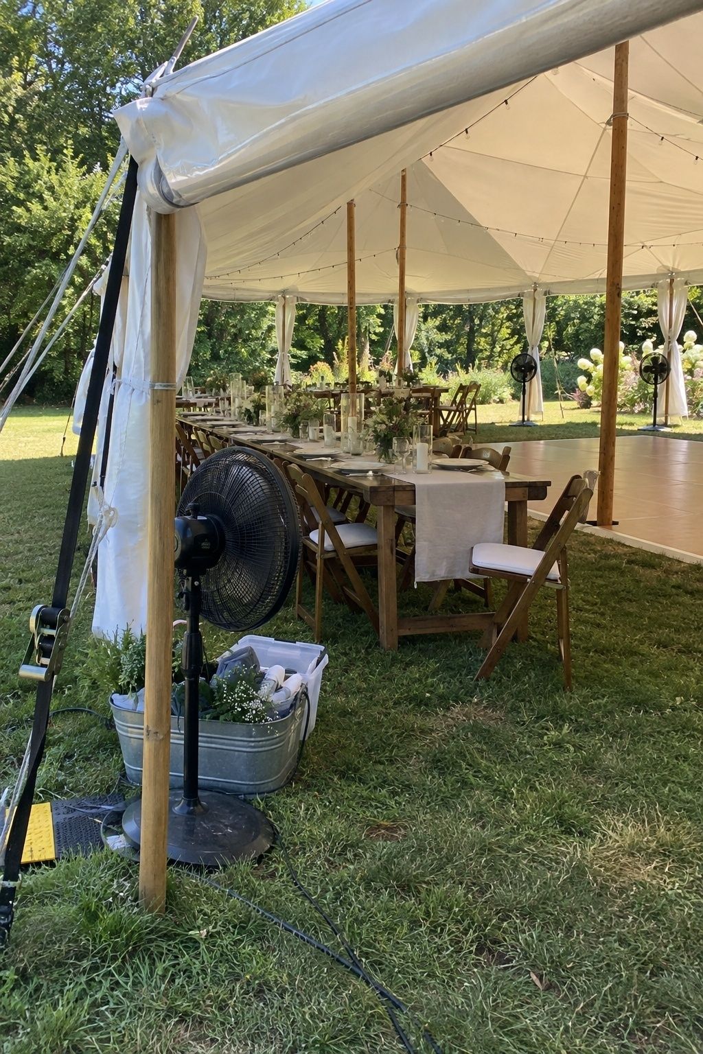 Open-sided small August wedding tent with shade, airflow fans, rolled sidewalls and a long reception table
