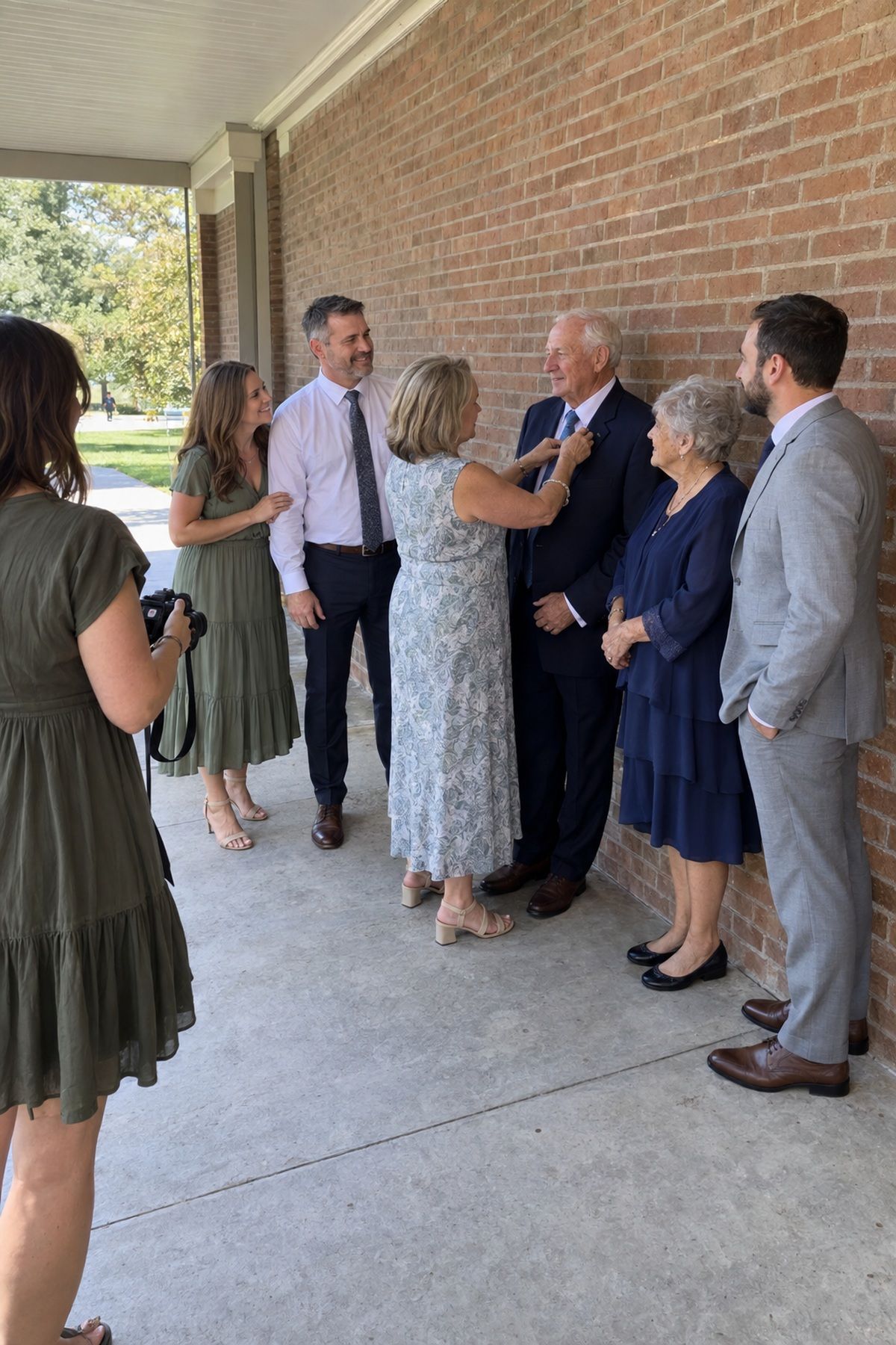 A multigenerational family gathers in a simple shaded location for August wedding photos.