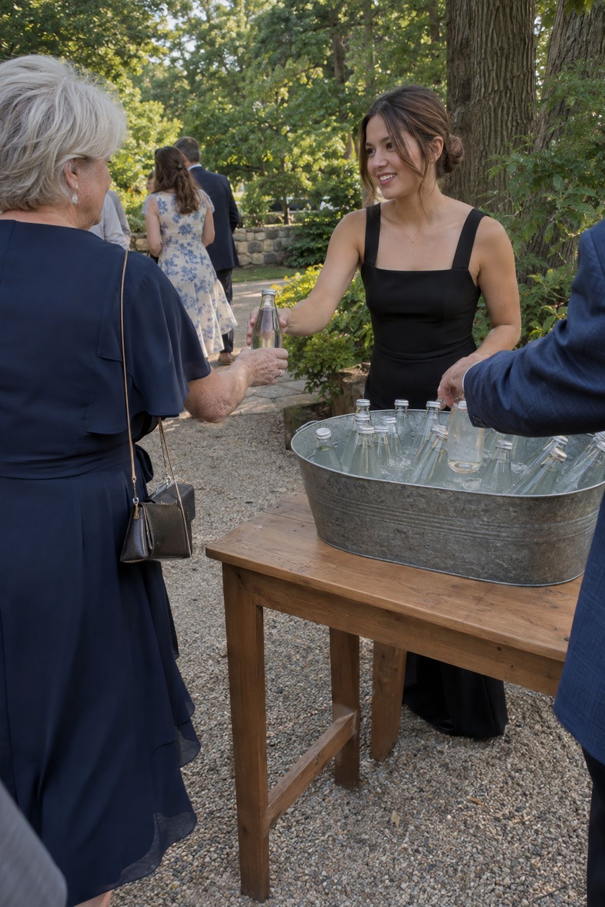 An attendant offers chilled water to an arriving guest at an August garden wedding.