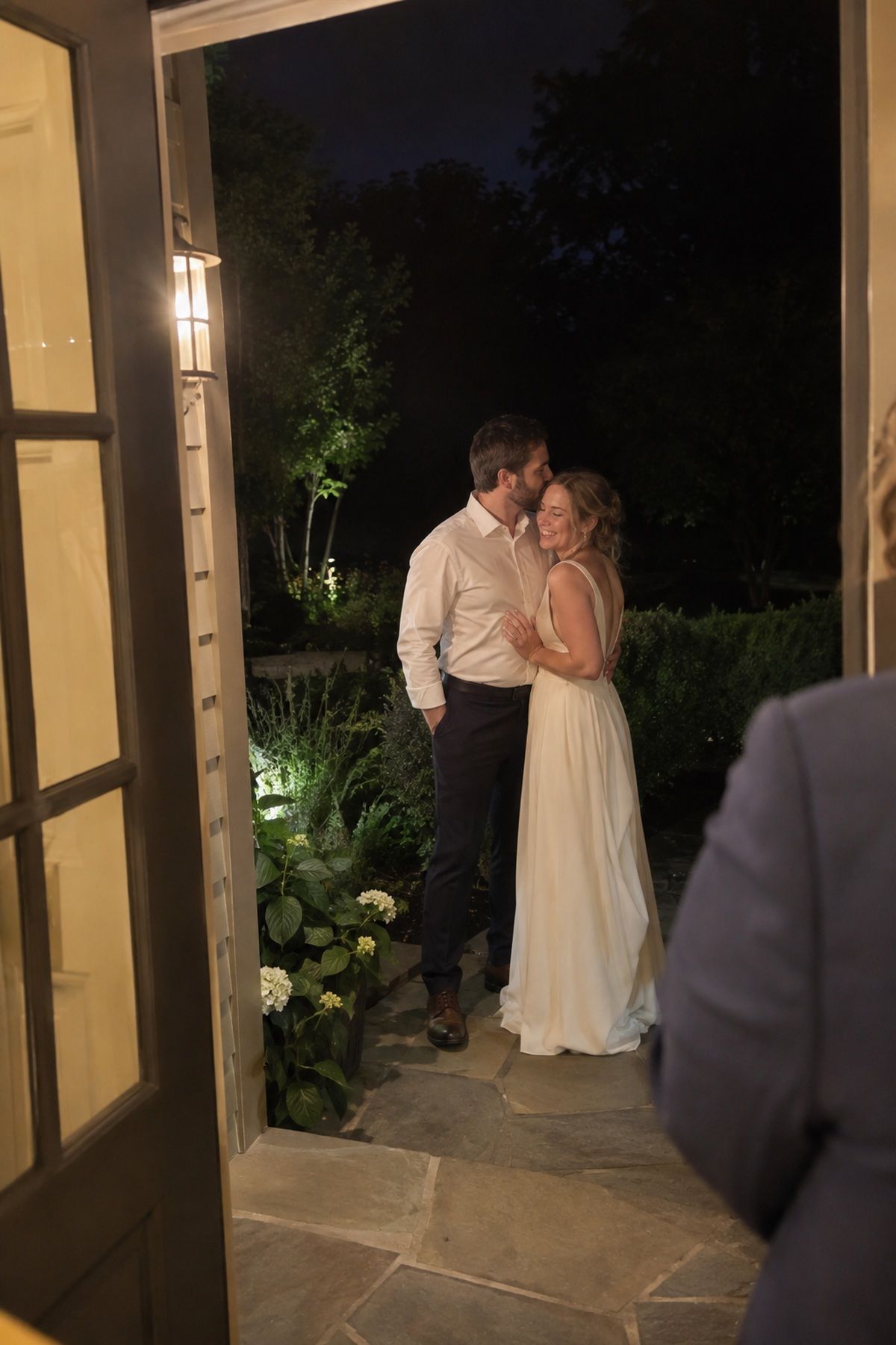 A couple pauses for an August wedding night portrait beside existing doorway light.