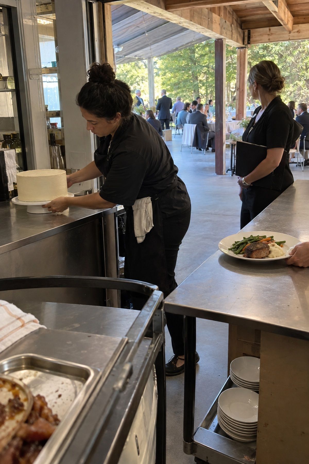 Catering staff prepare a plain cake and plated meal for photos before August wedding service.