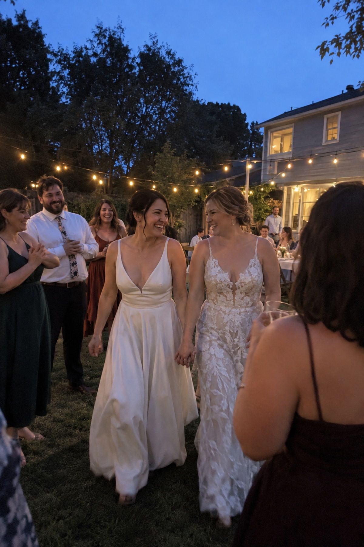 Two brides return hand in hand to their August wedding party at blue hour.