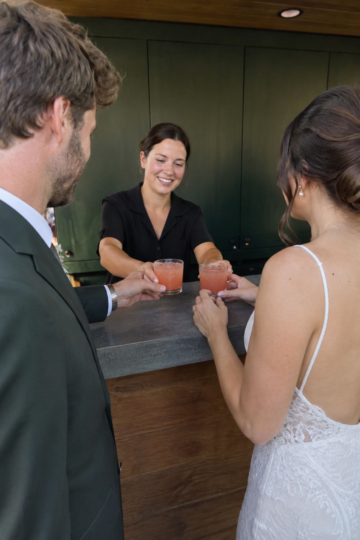 A bartender presents two matching late-summer signature drinks to newlyweds at a courtyard reception.