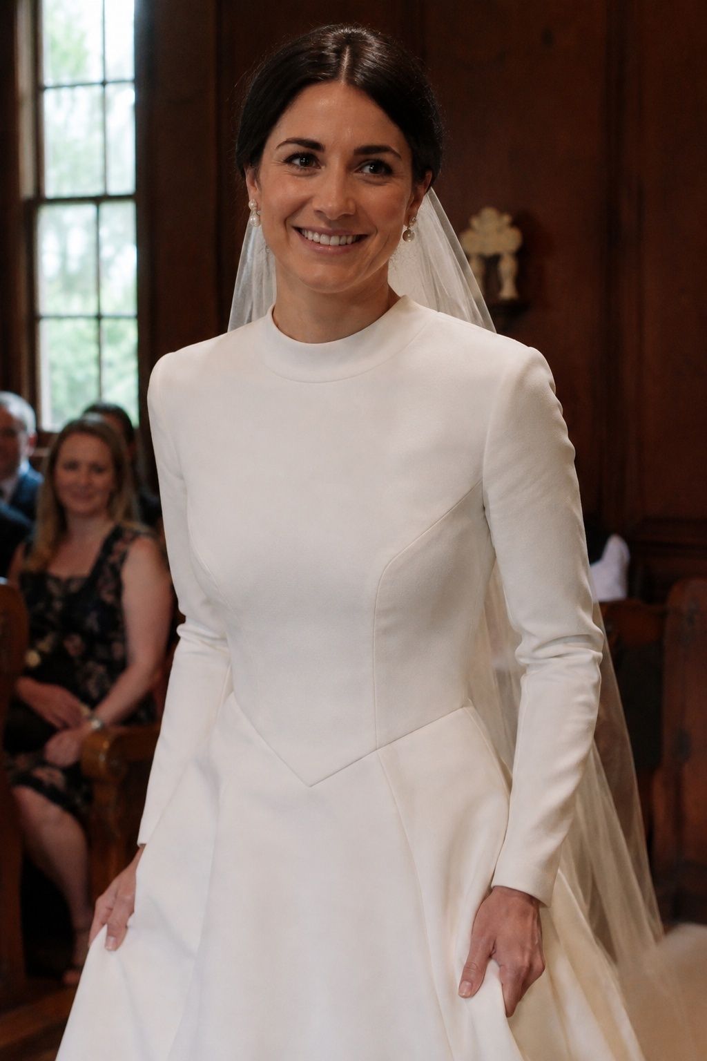 High-neck bridal gown with a pointed waist and pearl earrings