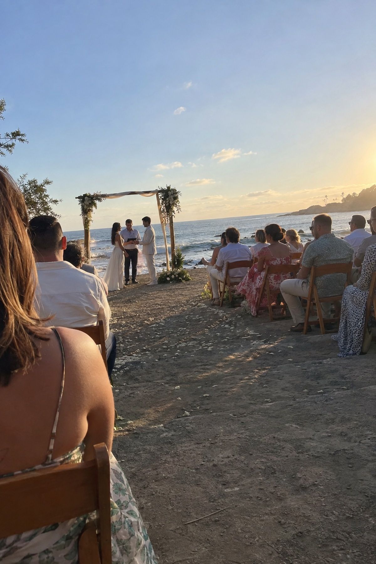 Guests sit comfortably during a late-afternoon beach wedding ceremony away from harsh midday sun.