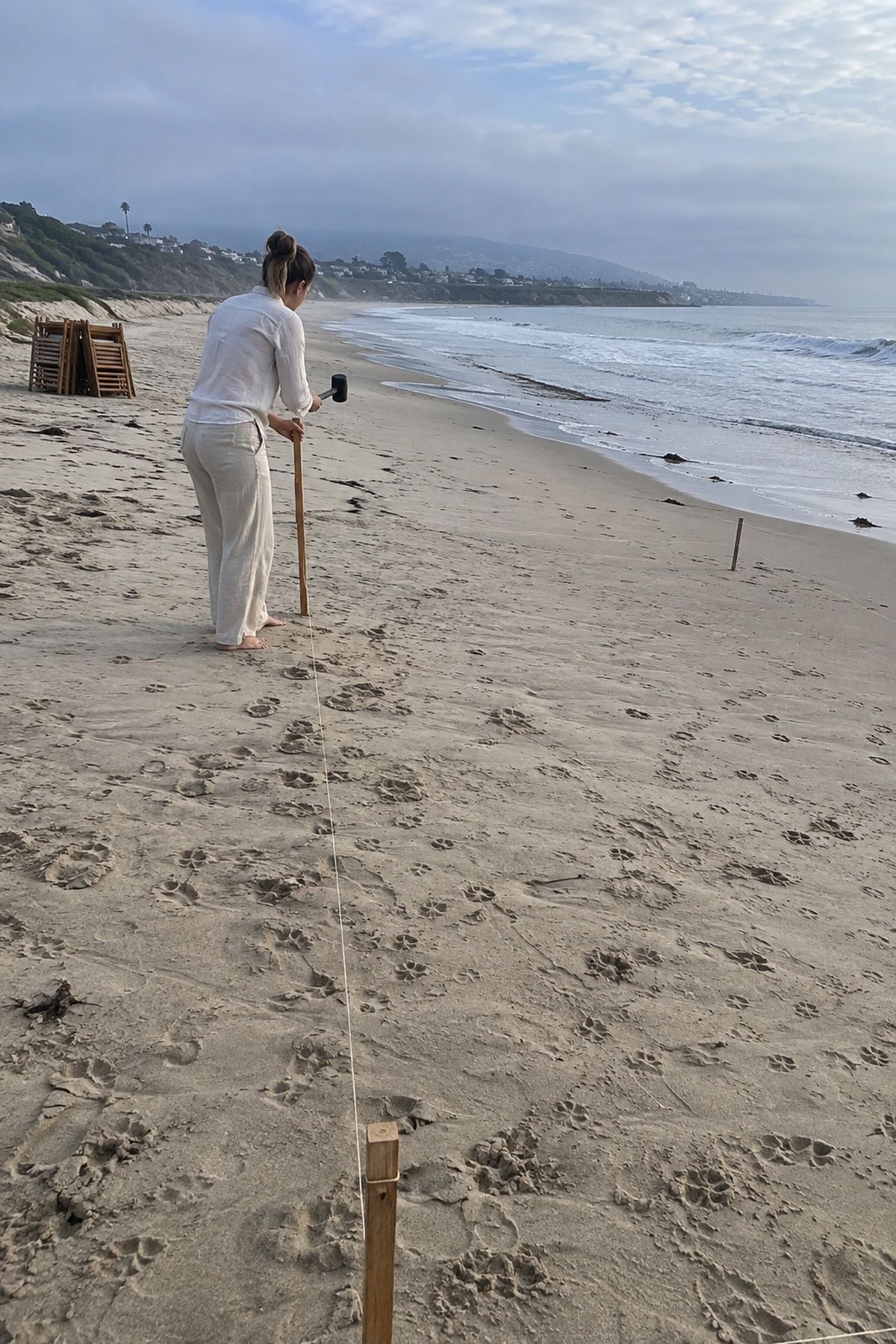 A coordinator marks a beach ceremony footprint well above the visible tide line.
