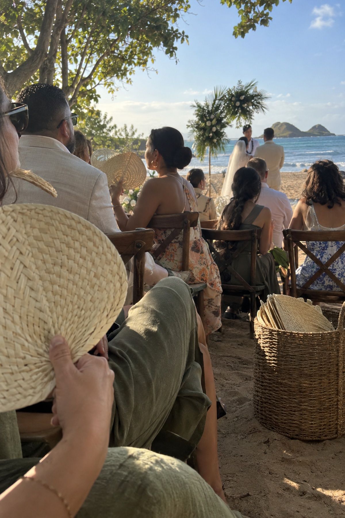 Beach wedding guests use sturdy handheld fans during a warm ceremony.