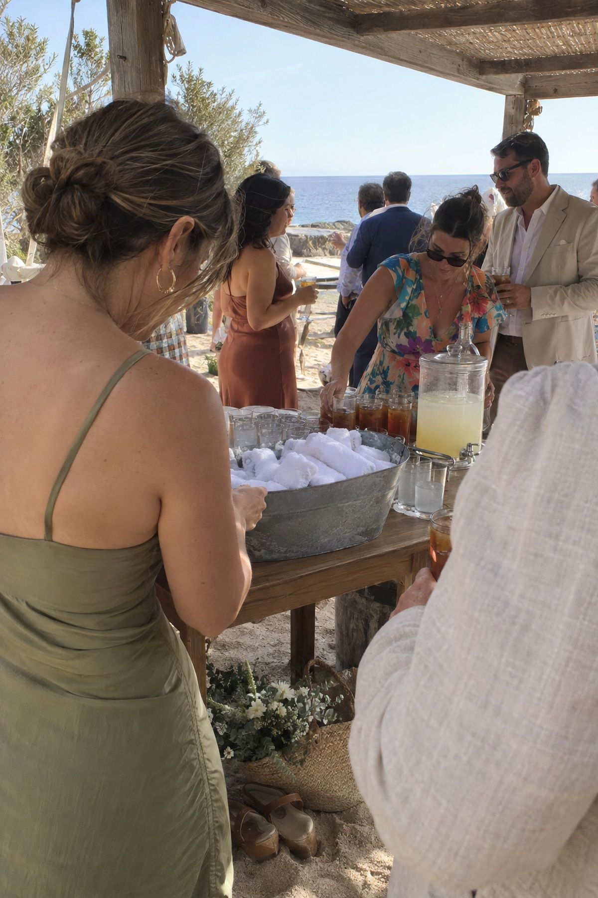 Beach wedding guests cool down in shade with chilled towels and cold drinks after the ceremony.