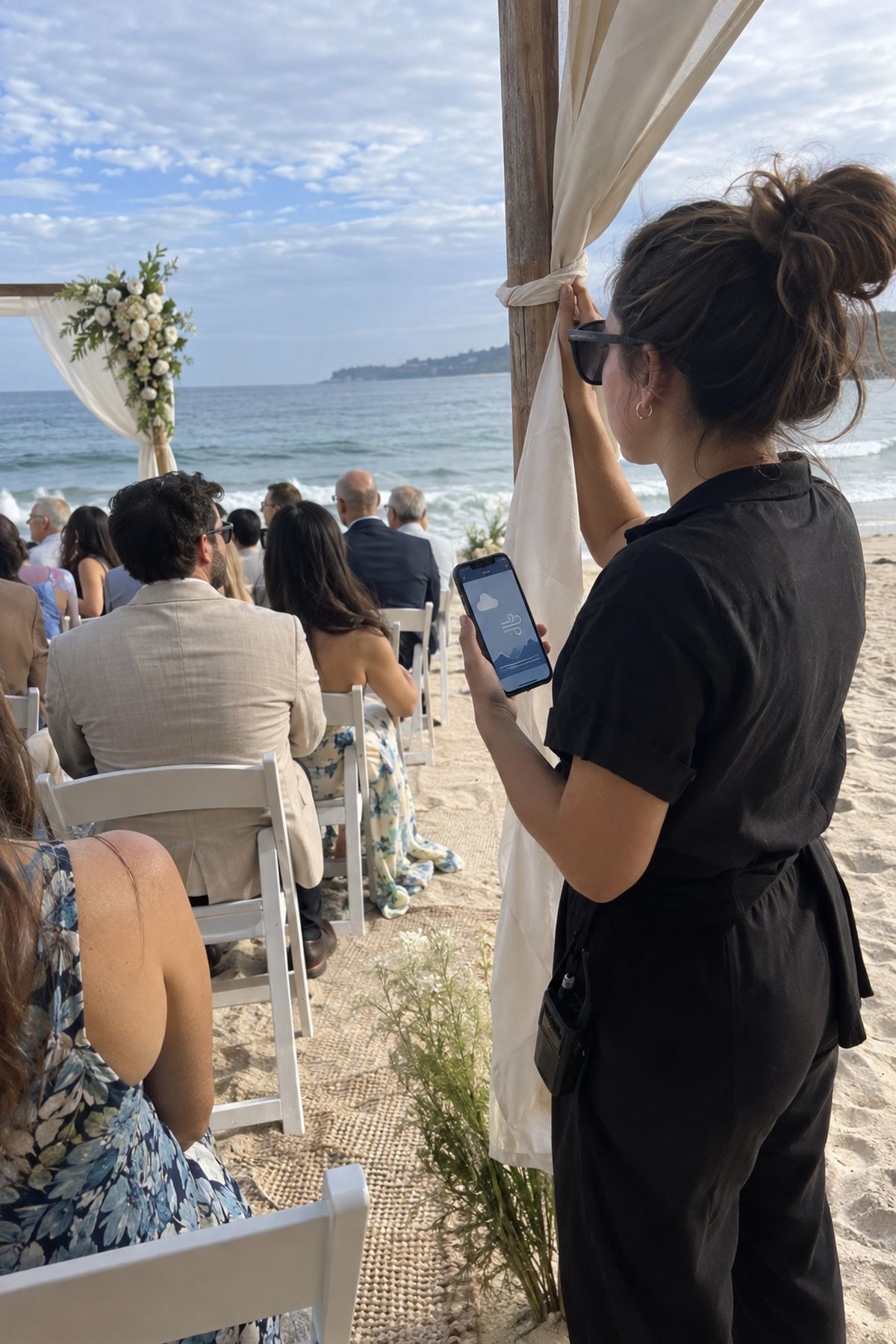 A beach wedding coordinator checks wind and tide conditions from the side of the ceremony.
