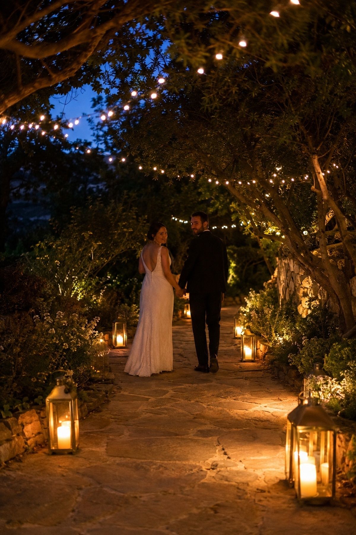 Newlyweds walking a lantern-lit garden path during blue hour