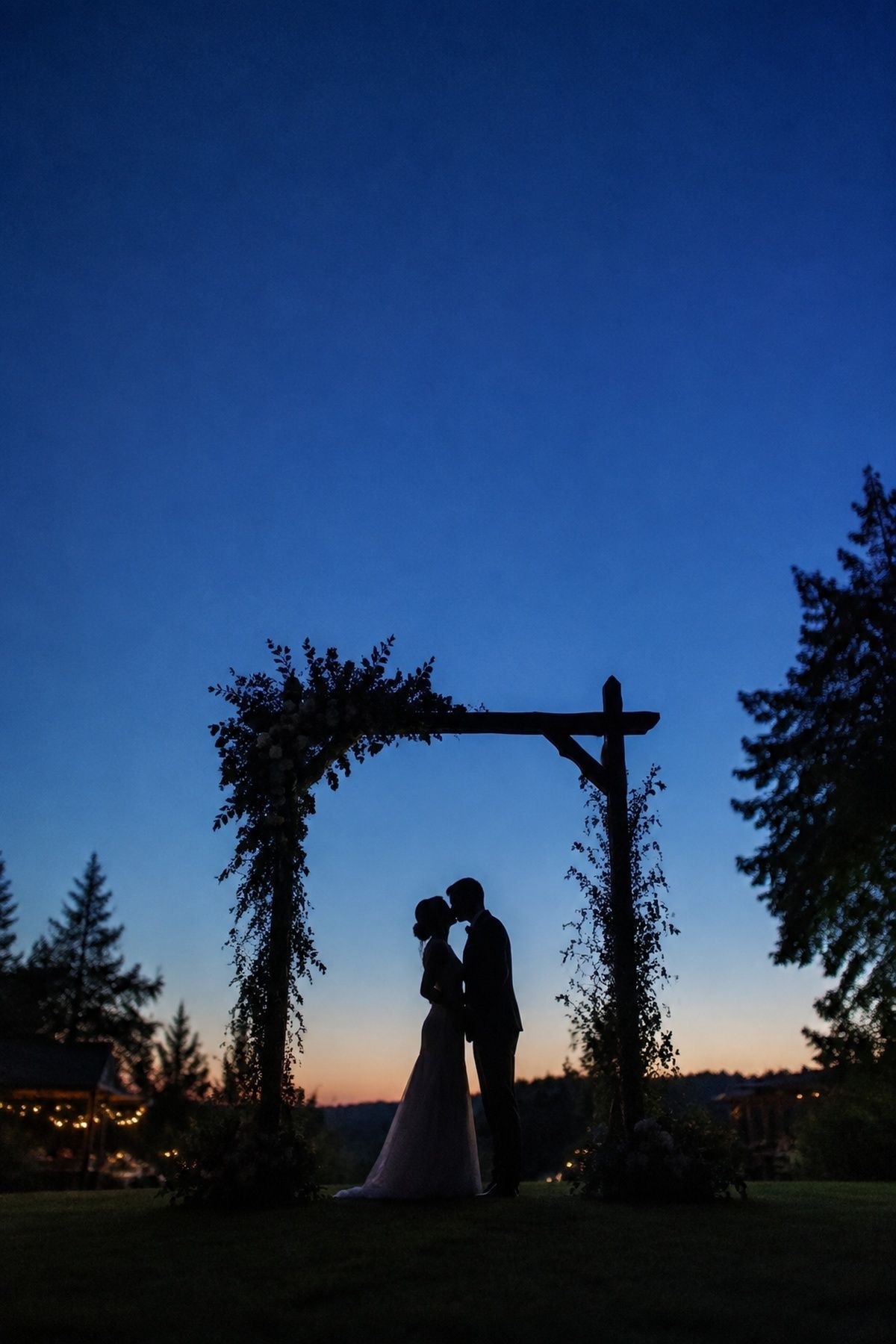 Newlywed silhouette framed beneath a floral ceremony arch at blue hour