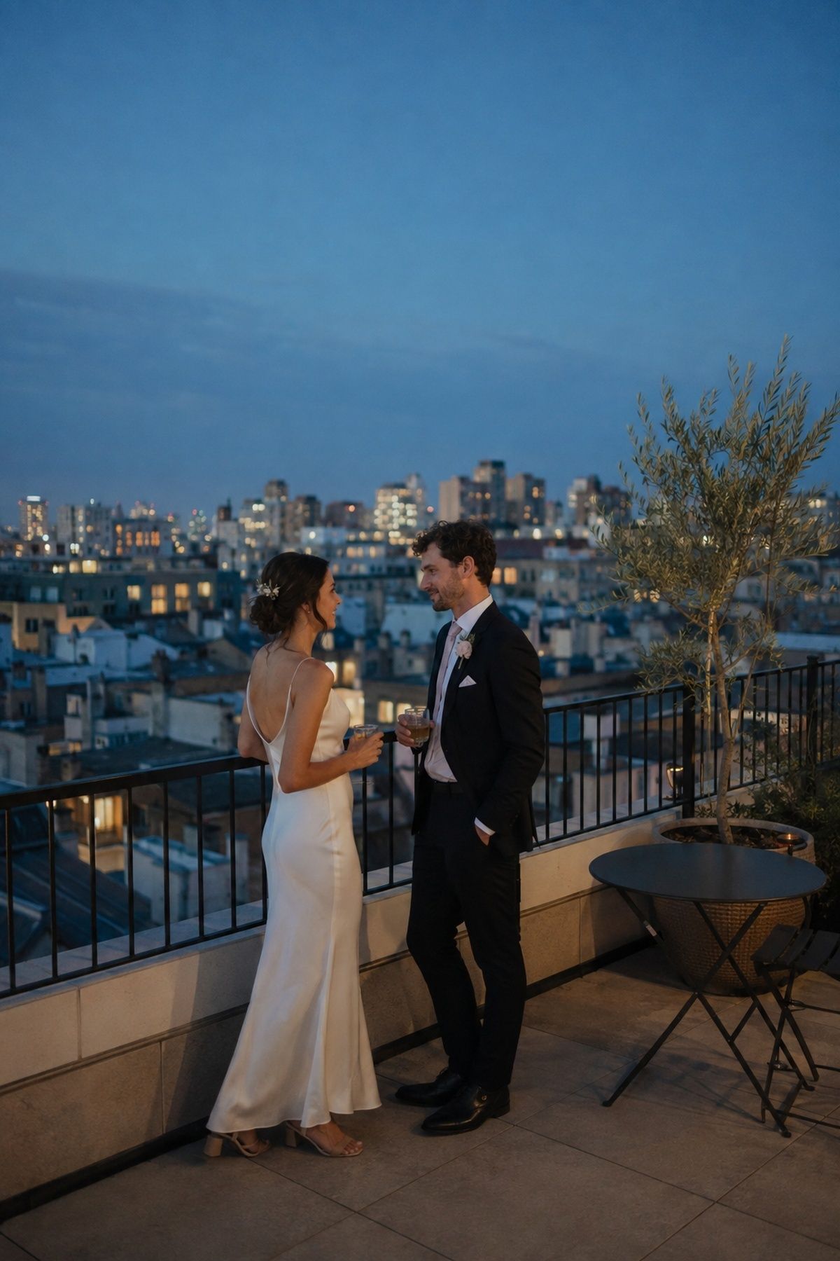 Newlyweds on a rooftop terrace with city lights during blue hour