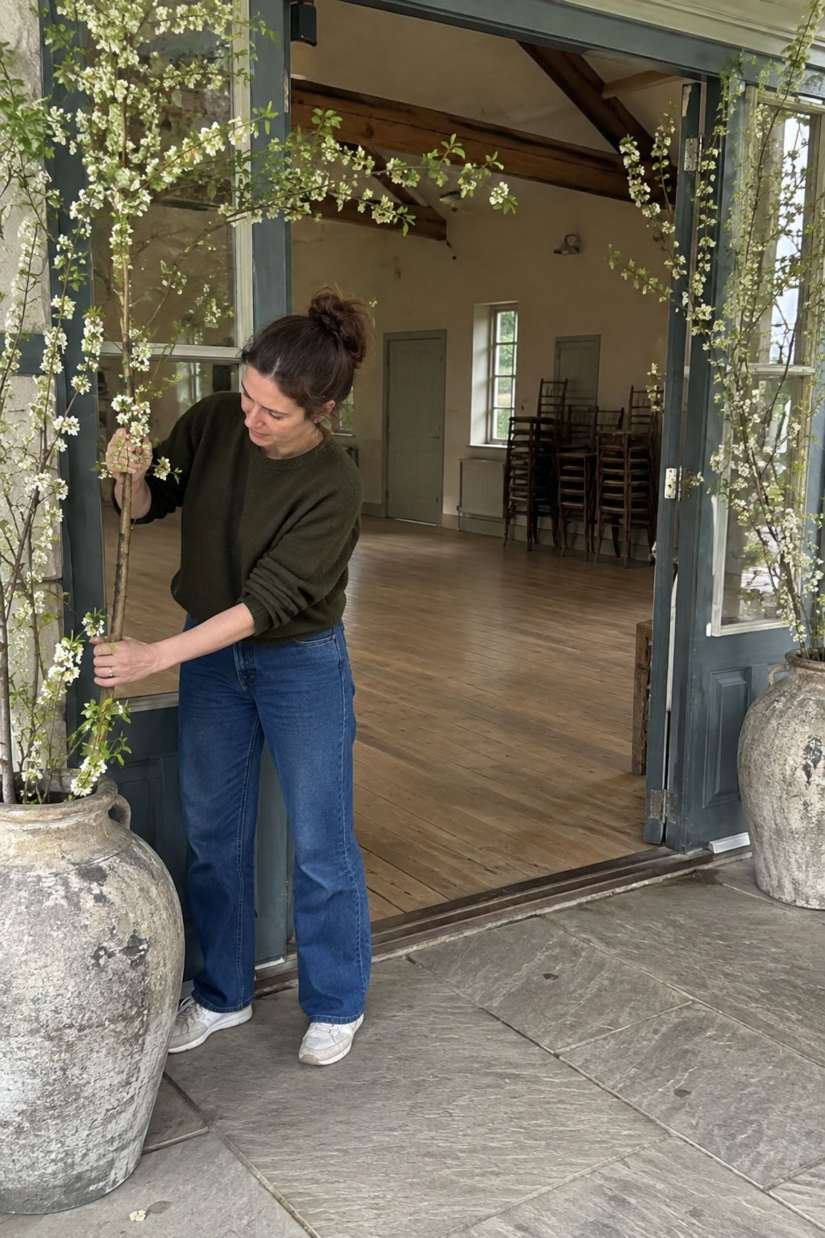 A coordinator secures tall flowering branches in weighted entrance vessels before wedding setup.