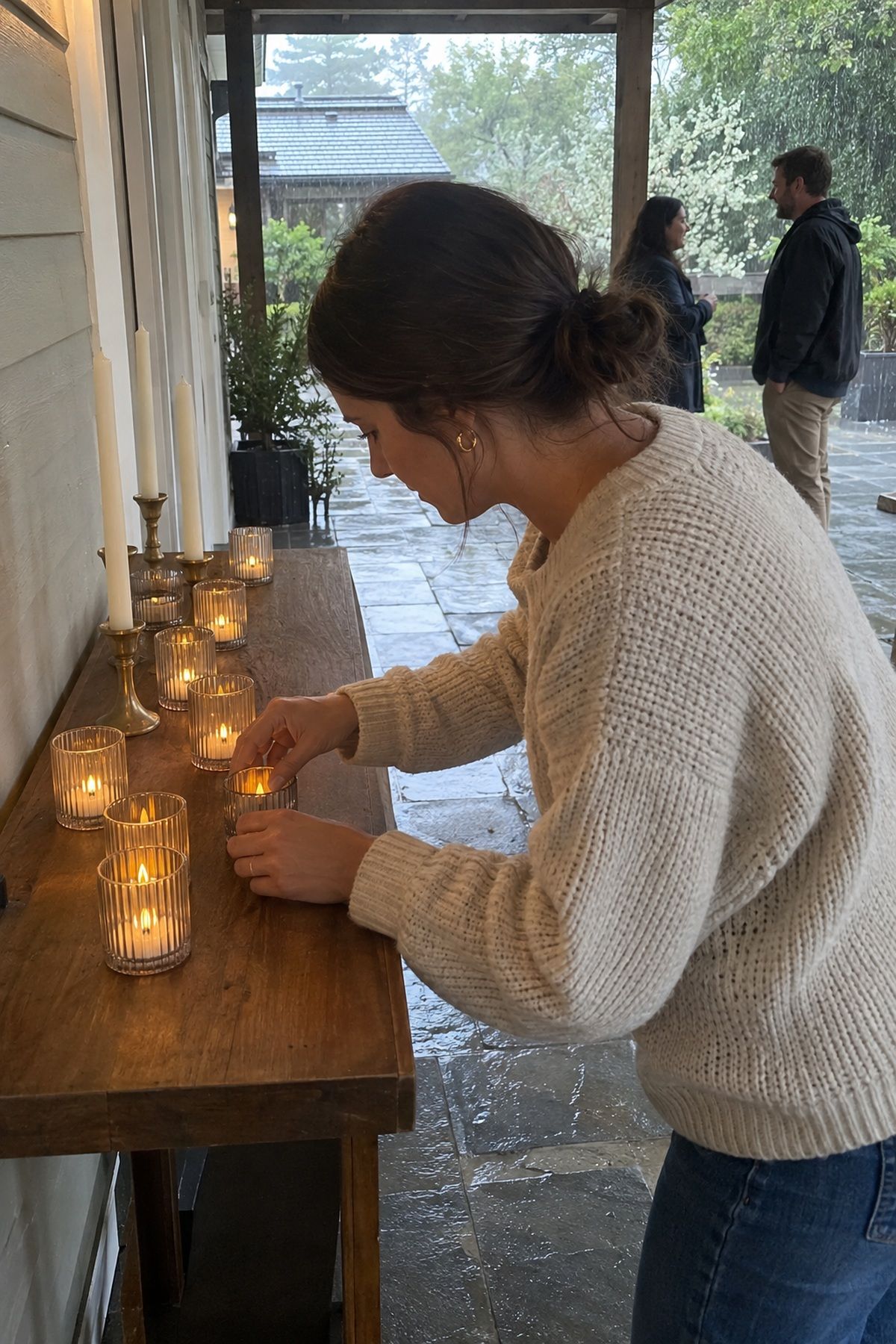 A helper turns on glass-covered LED votives while spring daylight and rain remain visible.