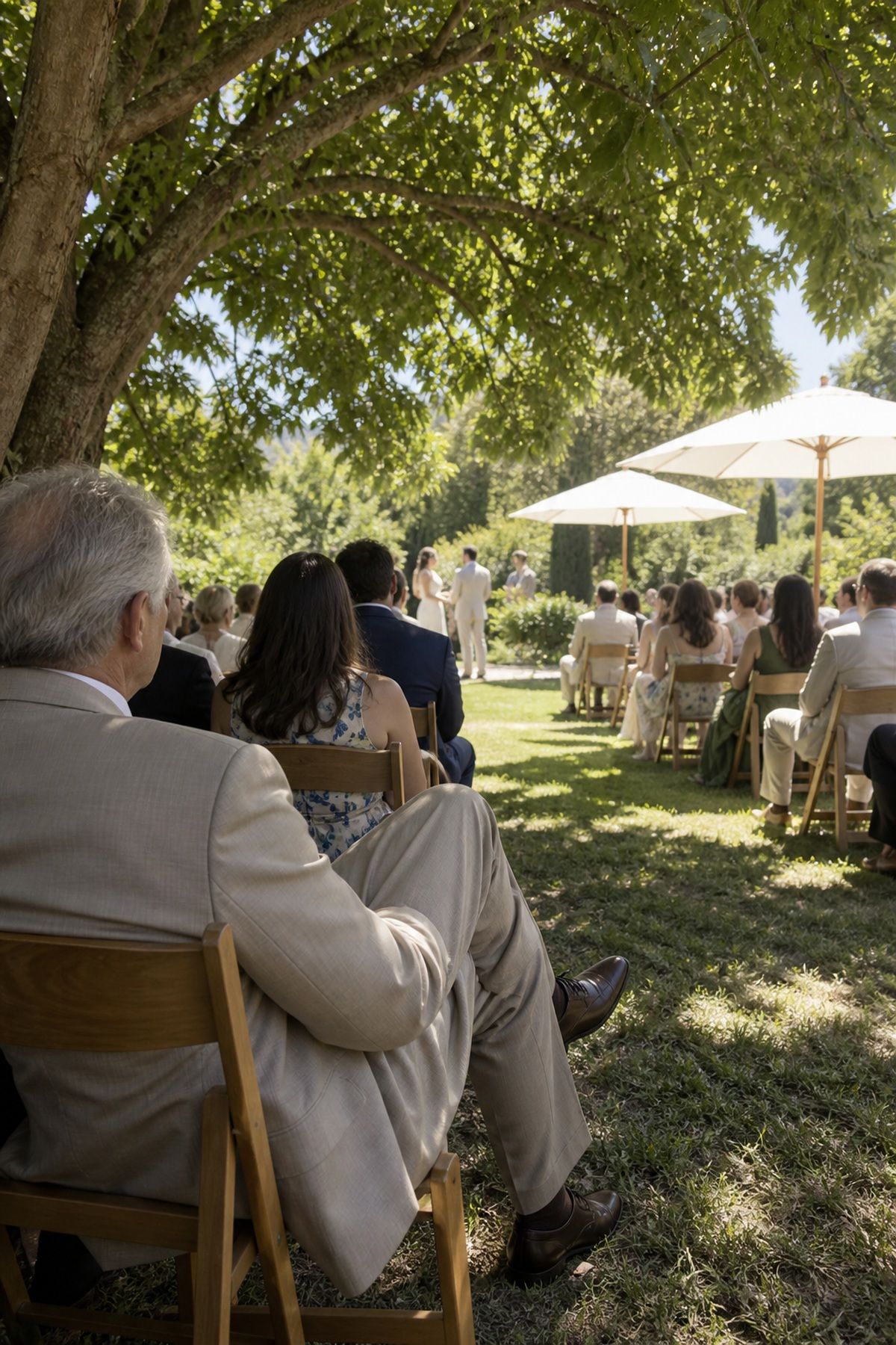 Guests relax beneath a mature tree and white umbrellas at a summer garden ceremony.