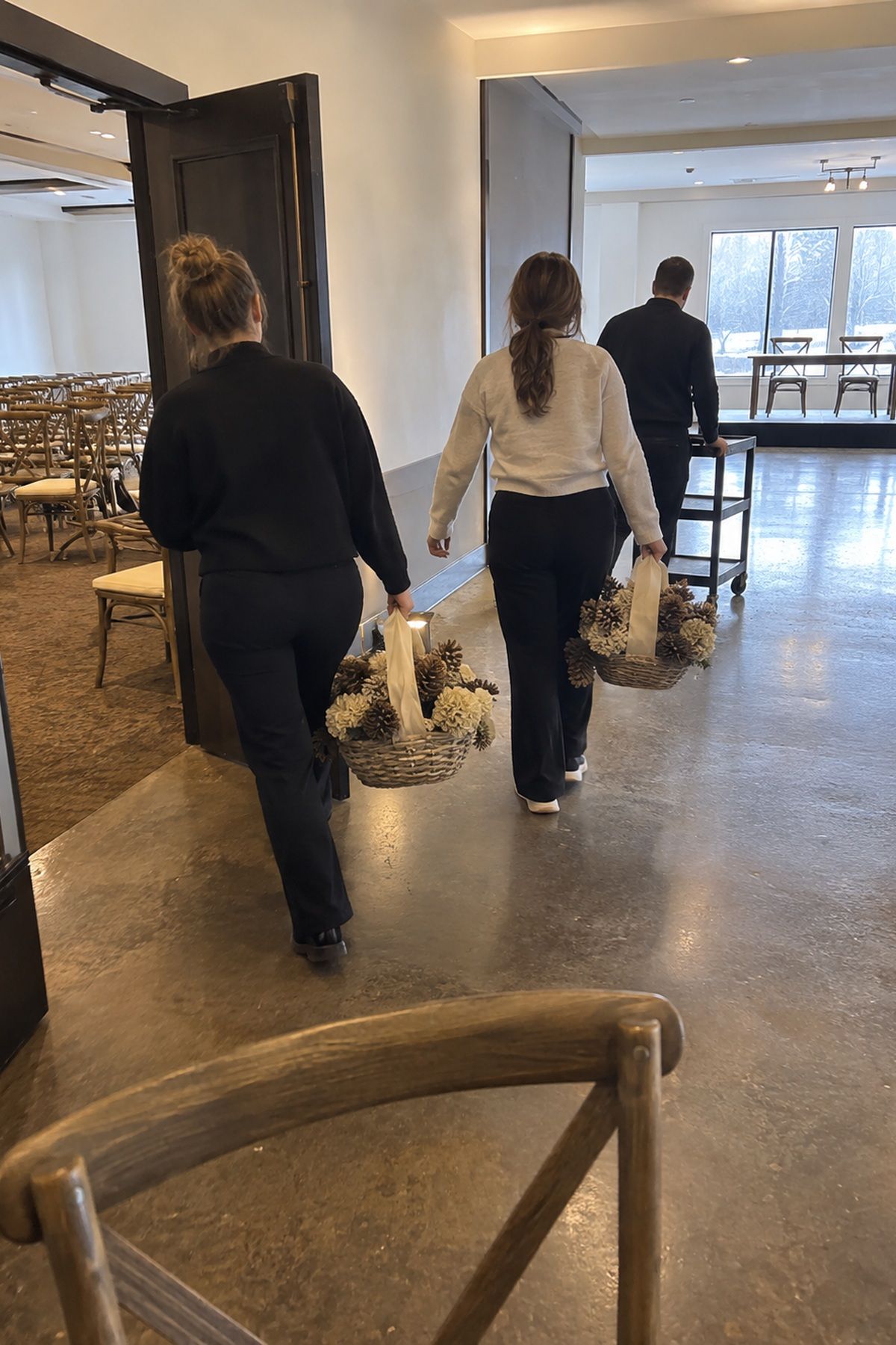 Wedding helpers carry lightweight ceremony baskets toward the dinner space for reuse.