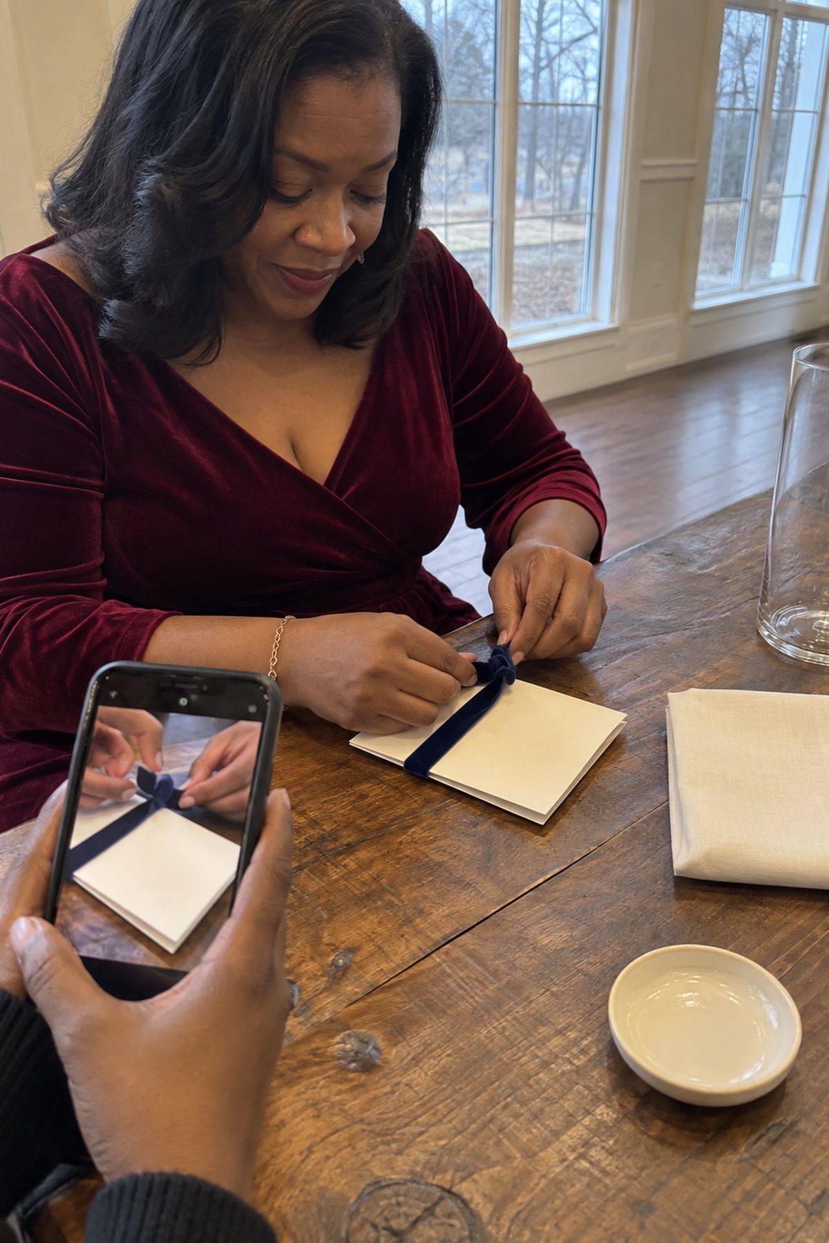 A wedding guest ties velvet ribbon around a cream card beside affordable linen, glass, and ring-dish details.