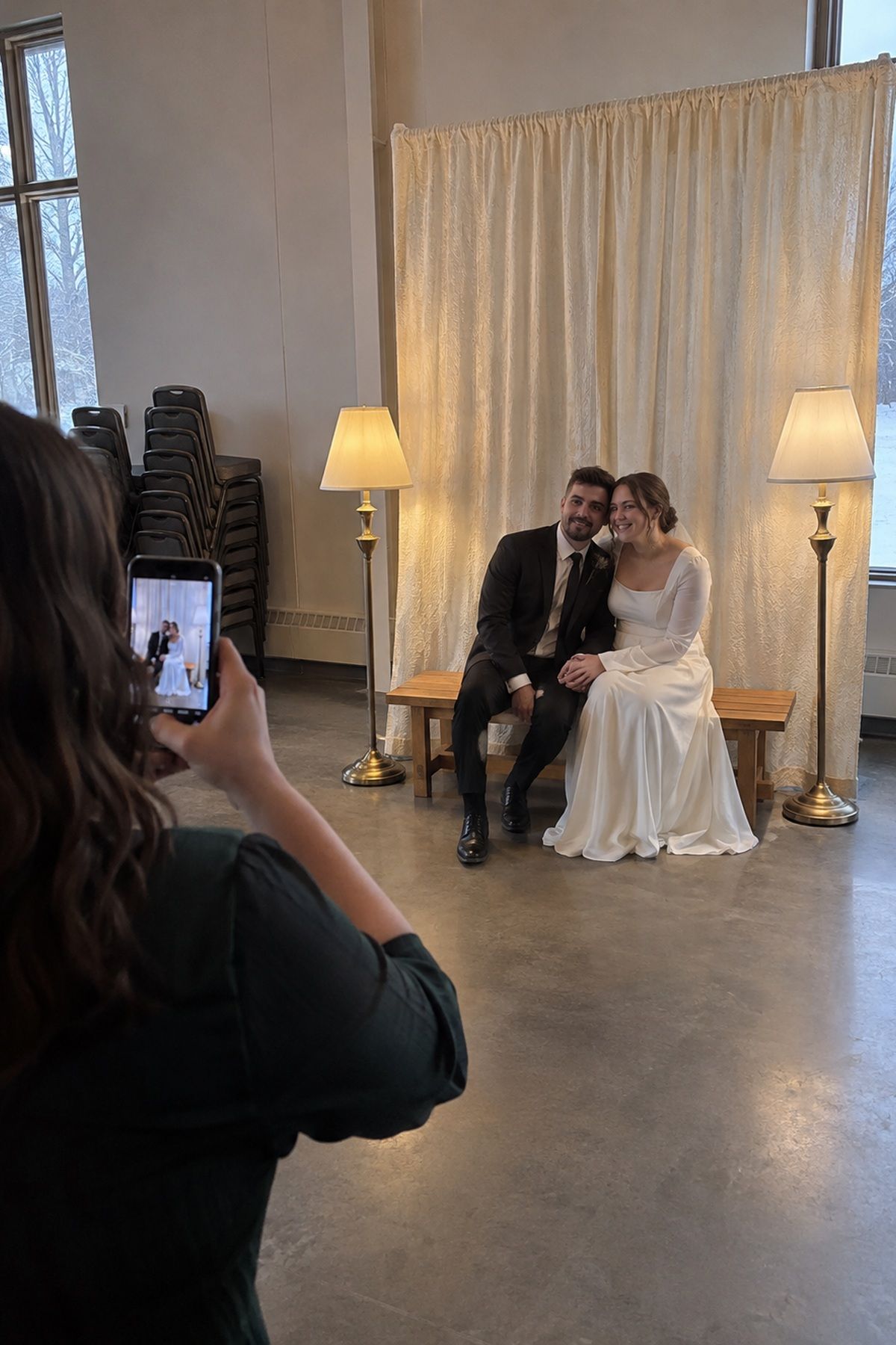 A guest photographs newlyweds in one simple winter wedding portrait corner while the rest of the hall stays plain.