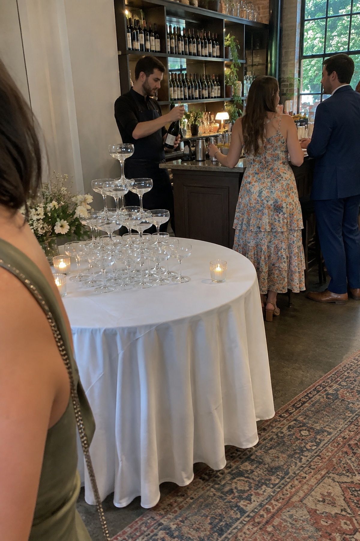 Low wide coupe glasses form a stable champagne tower beside a working wedding bar.