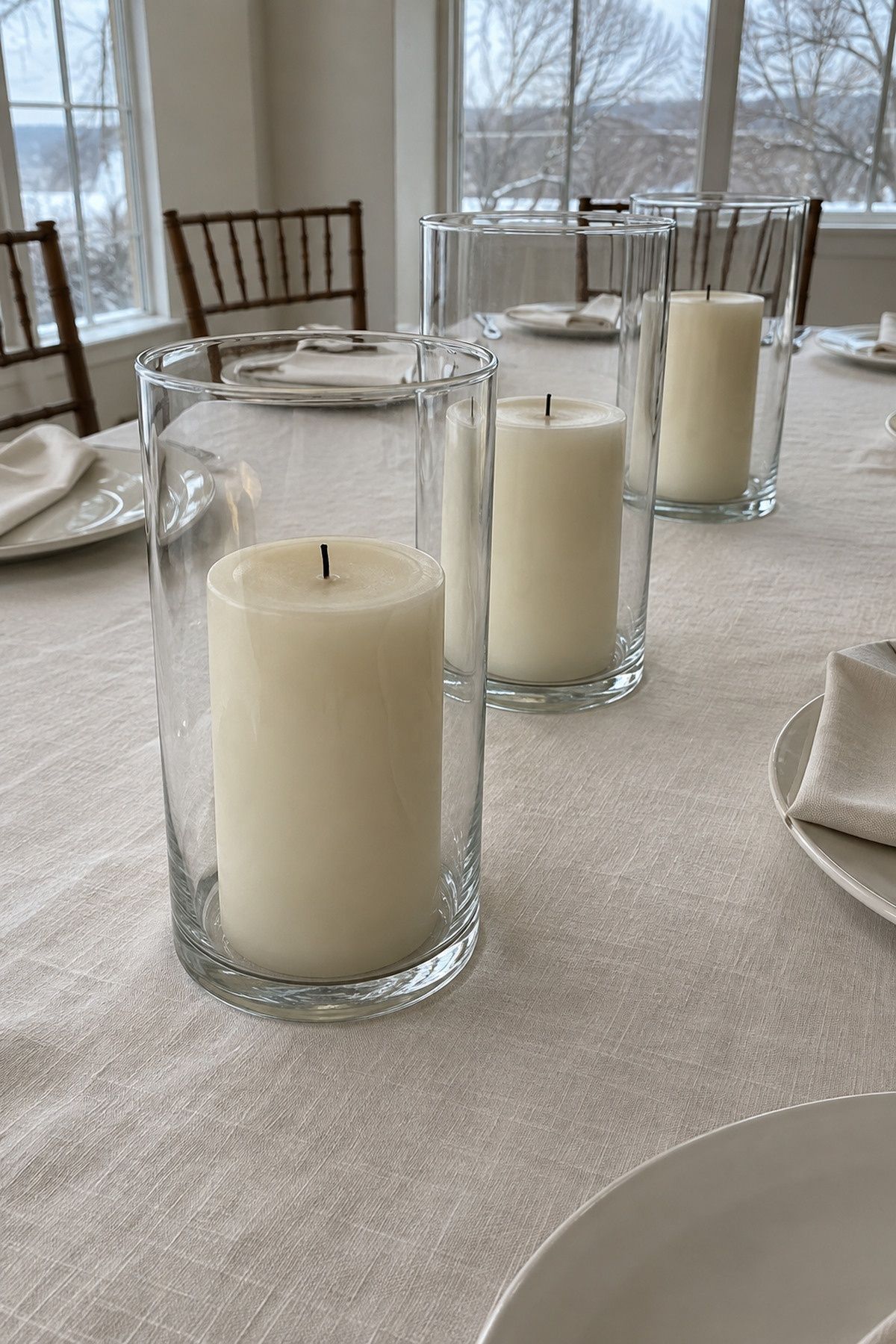 Clear glass hurricanes around unscented unlit pillars on the table center line at an intimate Christmas wedding reception