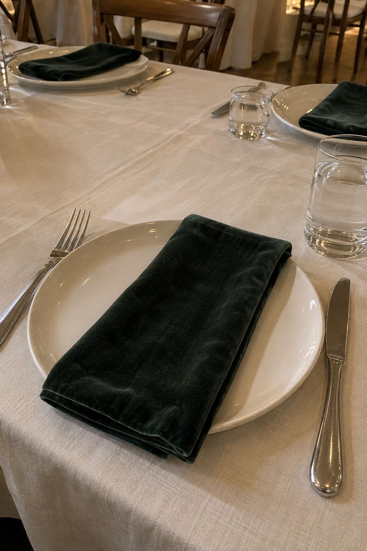 Forest-green velvet napkin across a simple ivory place setting at an intimate Christmas wedding reception