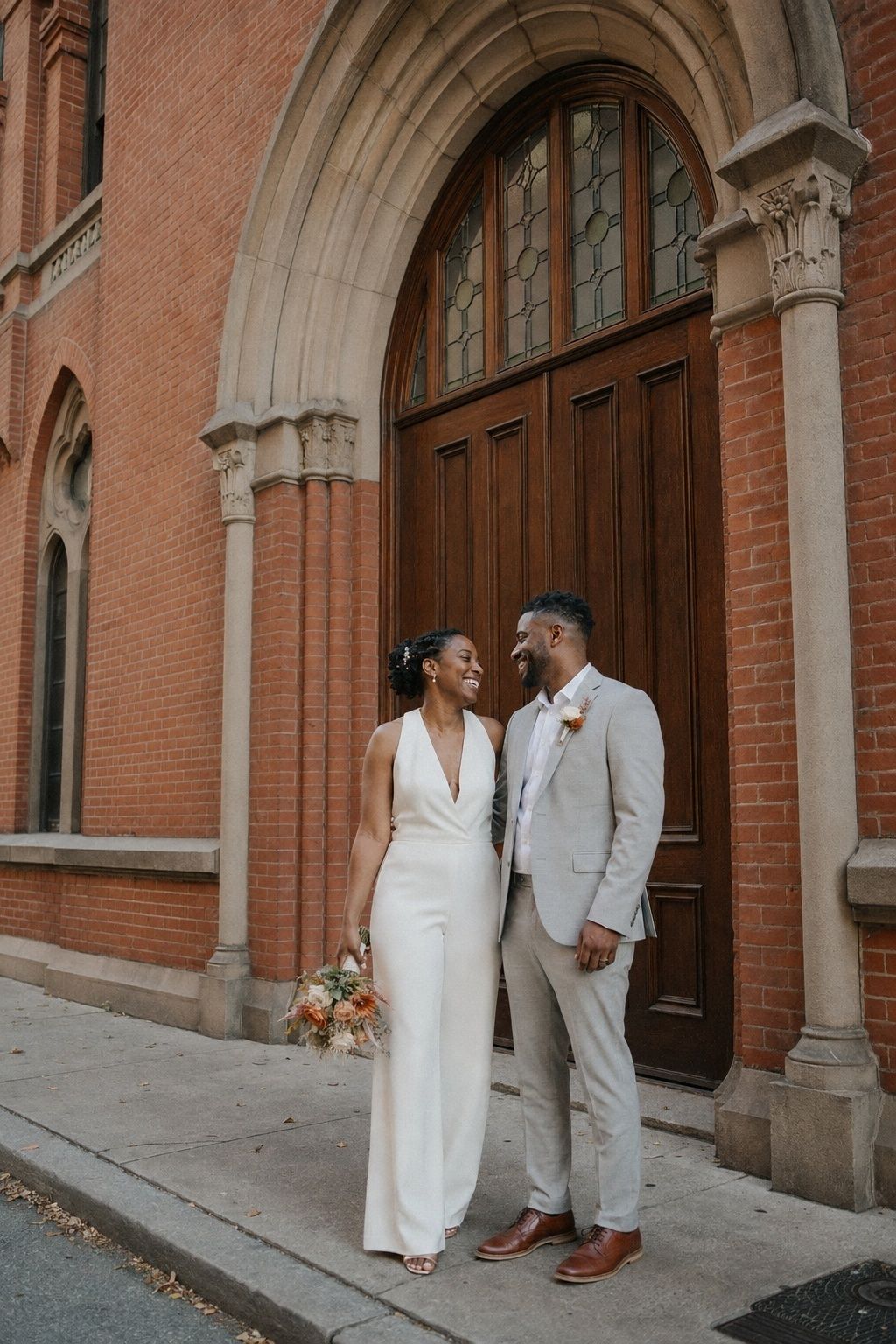 Newlyweds posing beside arched brick doorways near their ceremony venue.