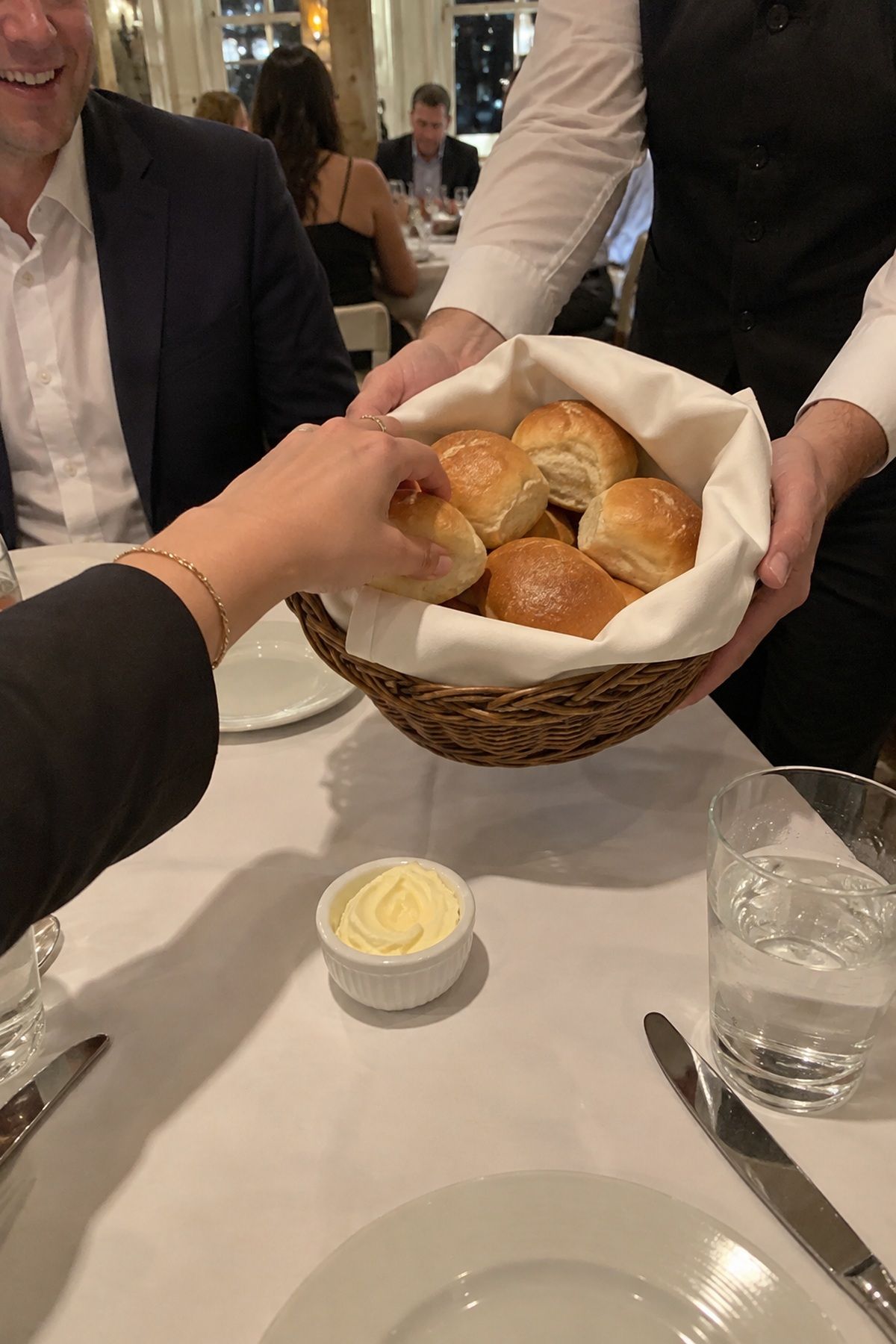 A wedding guest takes a warm roll from a fresh bread basket at dinner.