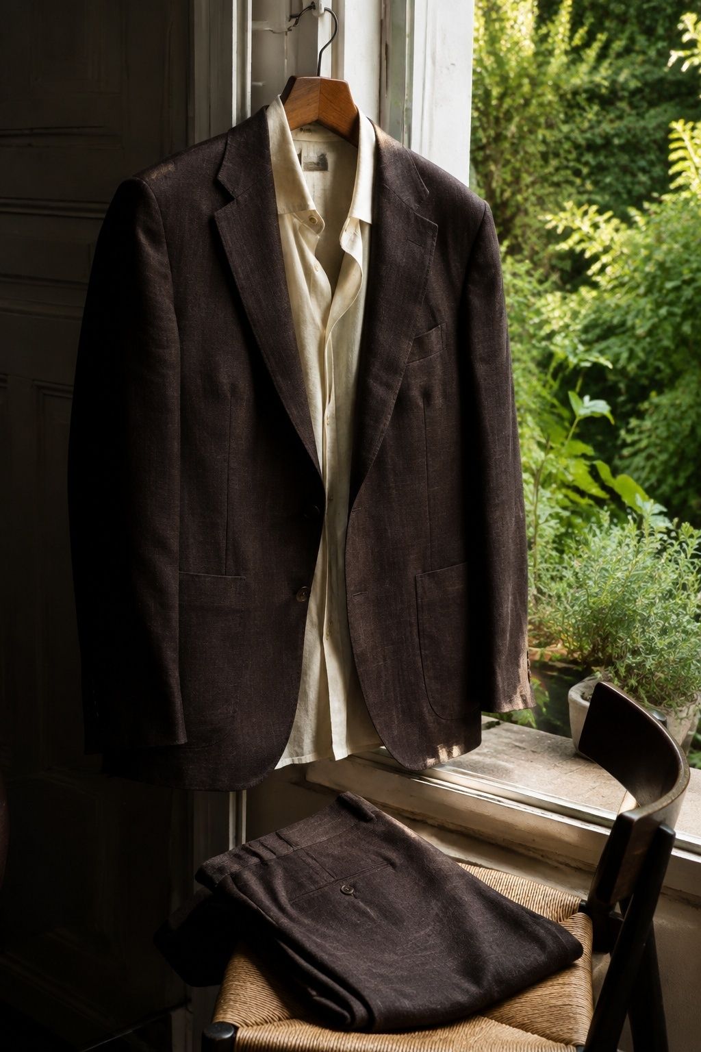 Lightweight dark brown linen-blend wedding suit beside a summer garden window.