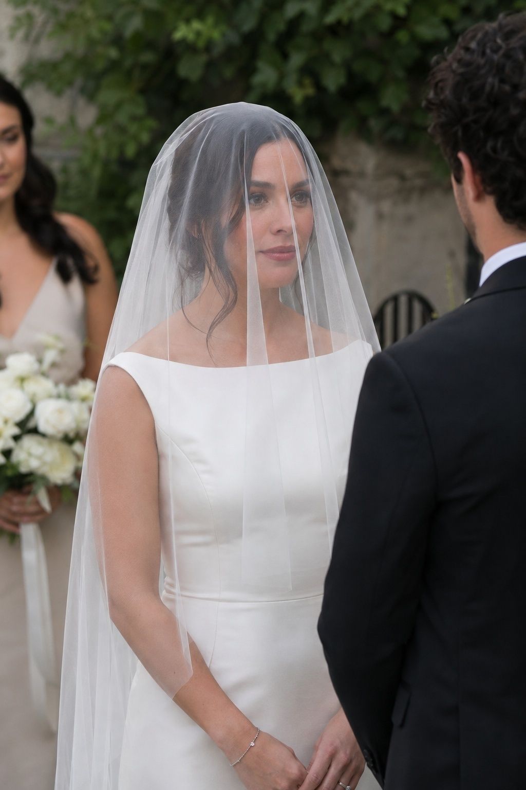 Three-quarter knee-up brunette bride in garden courtyard, plain sheer flat tulle over face and clean ivory satin bateau gown