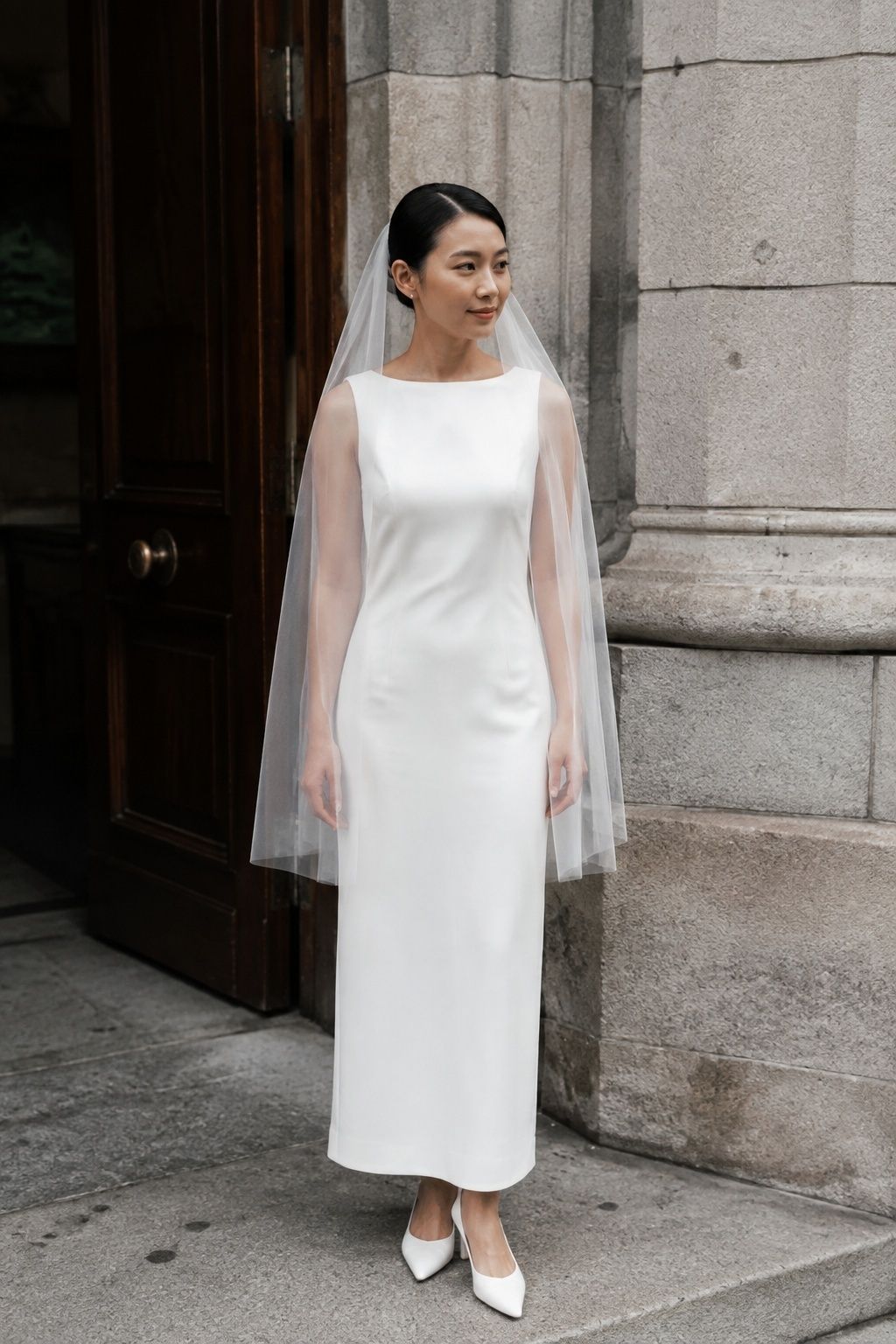 Full-length East Asian bride beside registry-office doorway, fingertip drop veil ending exactly at relaxed fingertips, short manageable tulle and simple ivory gown