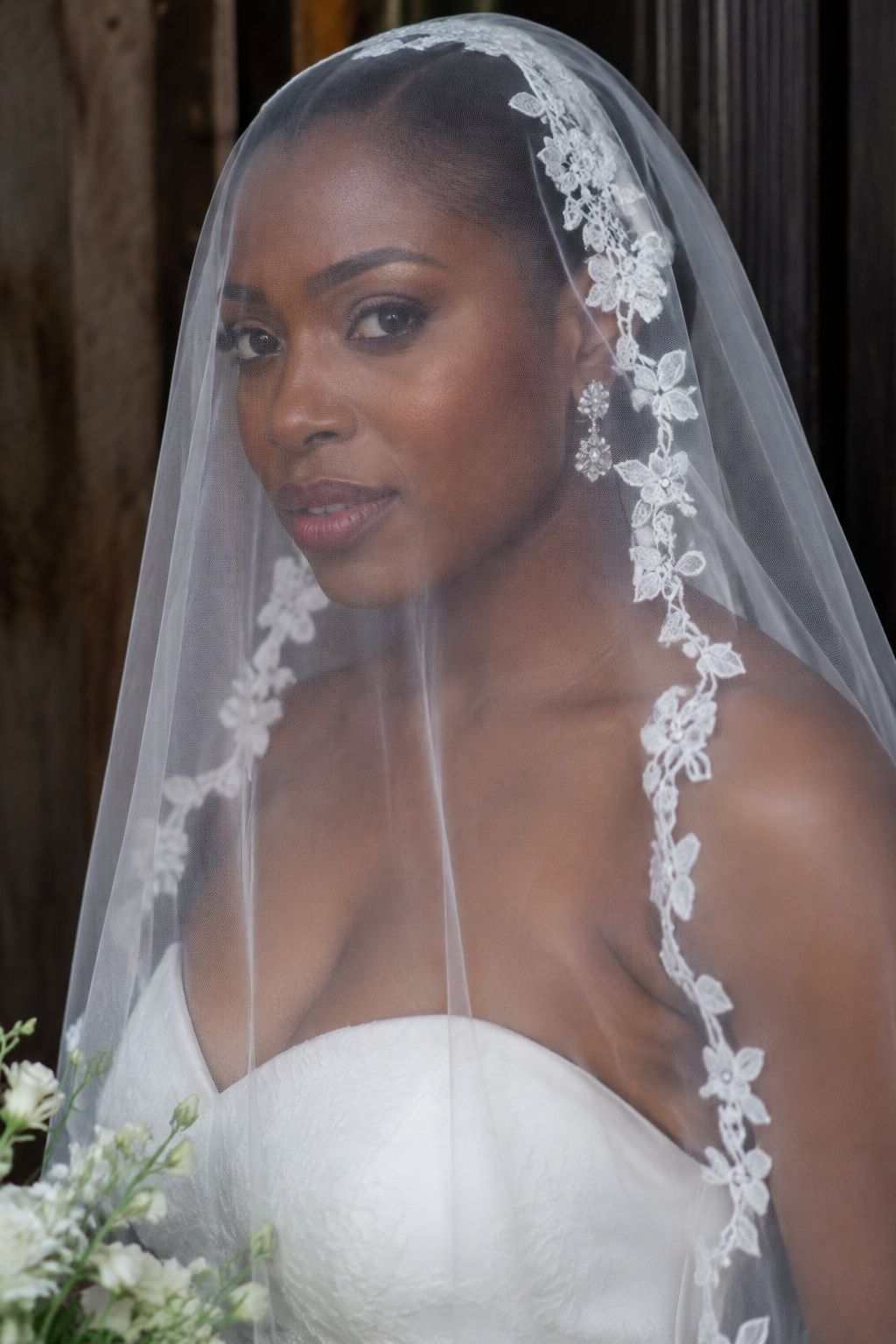 Close front portrait of Black bride with sheer face blusher and delicate narrow floral lace edging framing face without obscuring eyes, smooth crown
