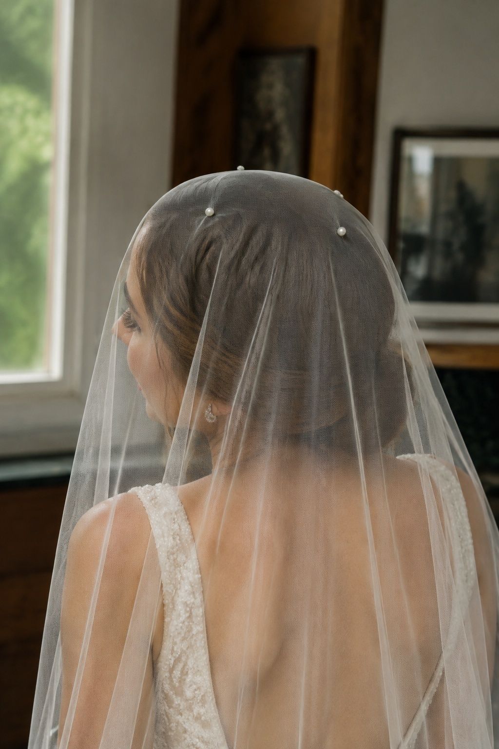 Close rear three-quarter crown detail, three small pearl pins symmetrically securing flat transparent tulle over chestnut hair, hidden comb and no gathers
