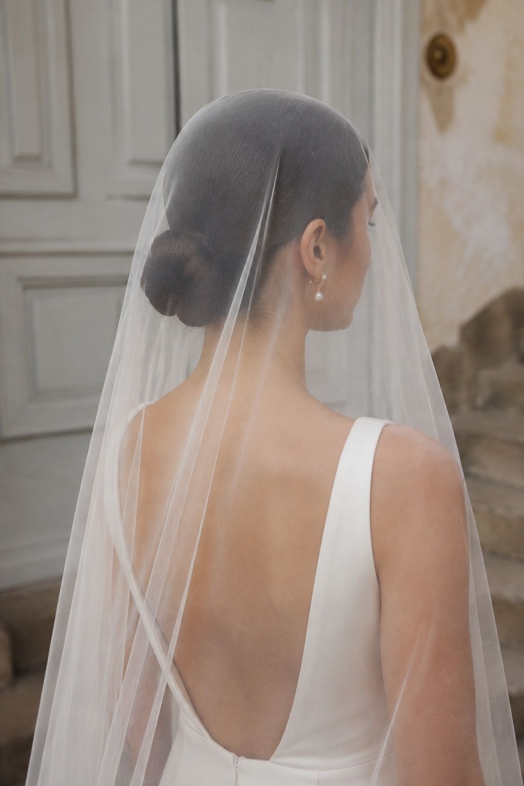 Rear shoulder portrait of bride with sleek low dark bun at nape, sheer tulle resting flat across crown and flowing smoothly around bun