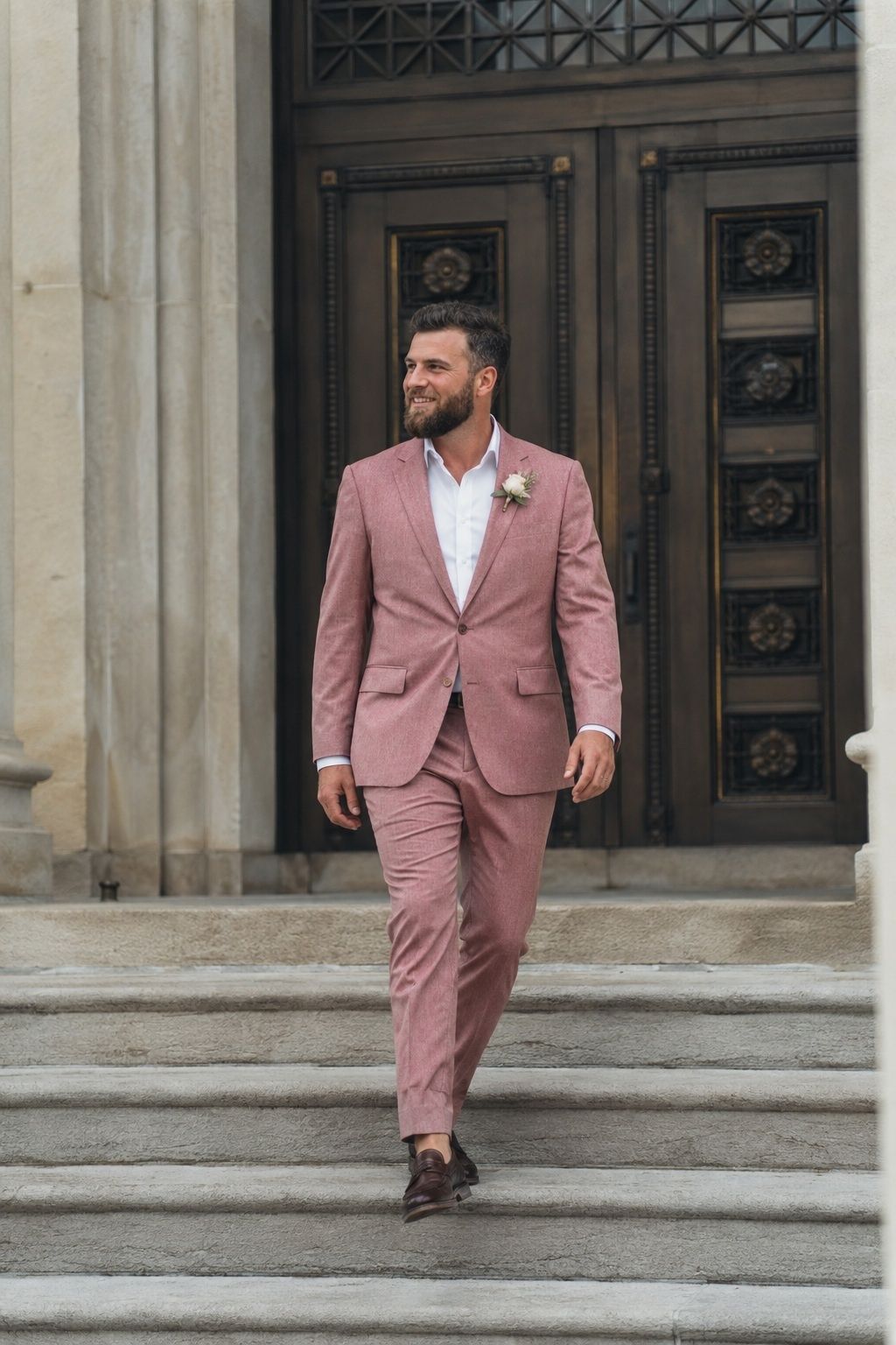 Groom in a dusty rose suit walking down stone city hall steps.