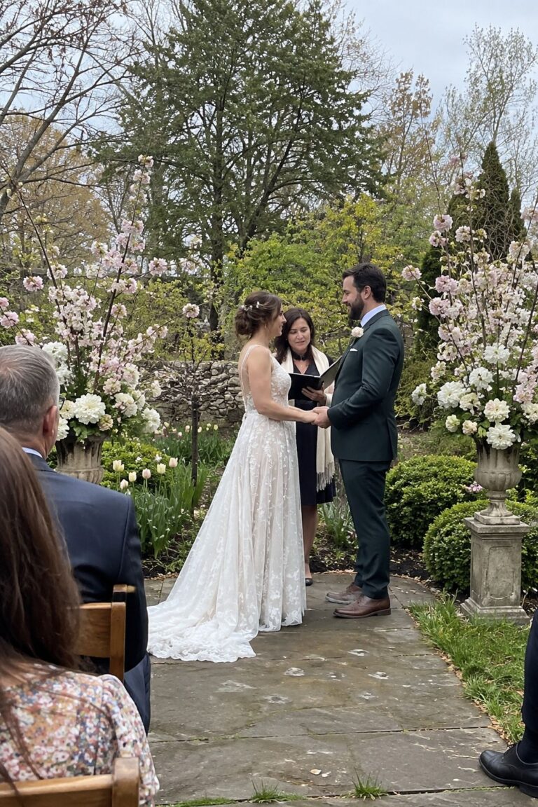 A couple exchange vows beside blooming branches at a spring garden ceremony.