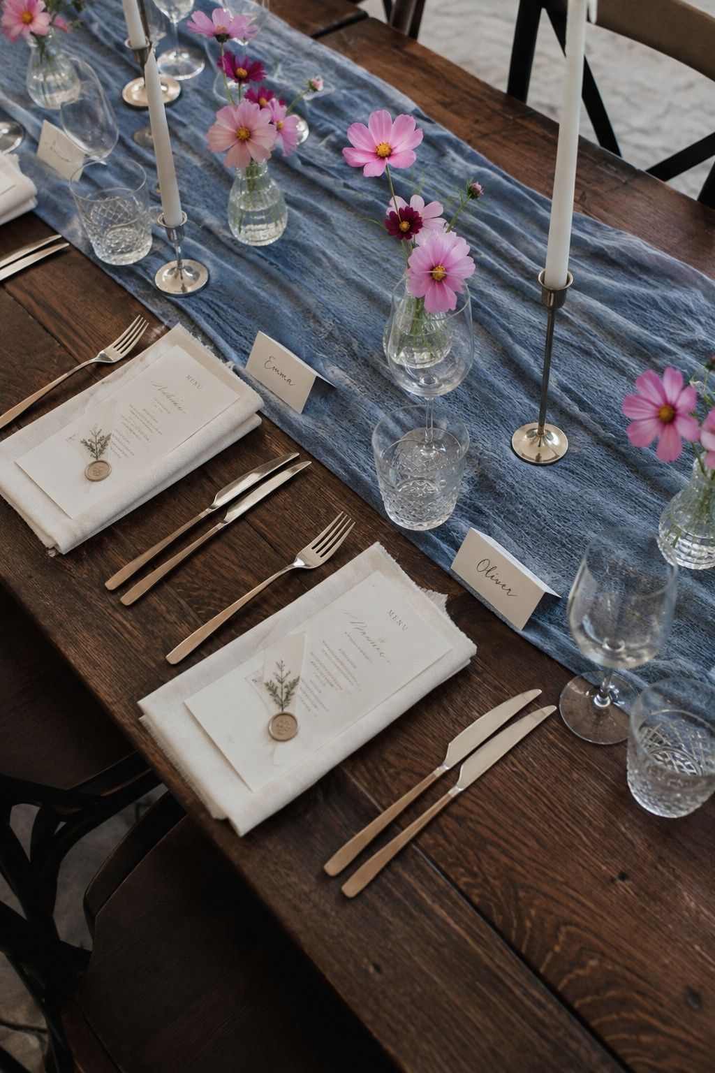 Wedding place settings with a blue runner, pink cosmos and cream place cards