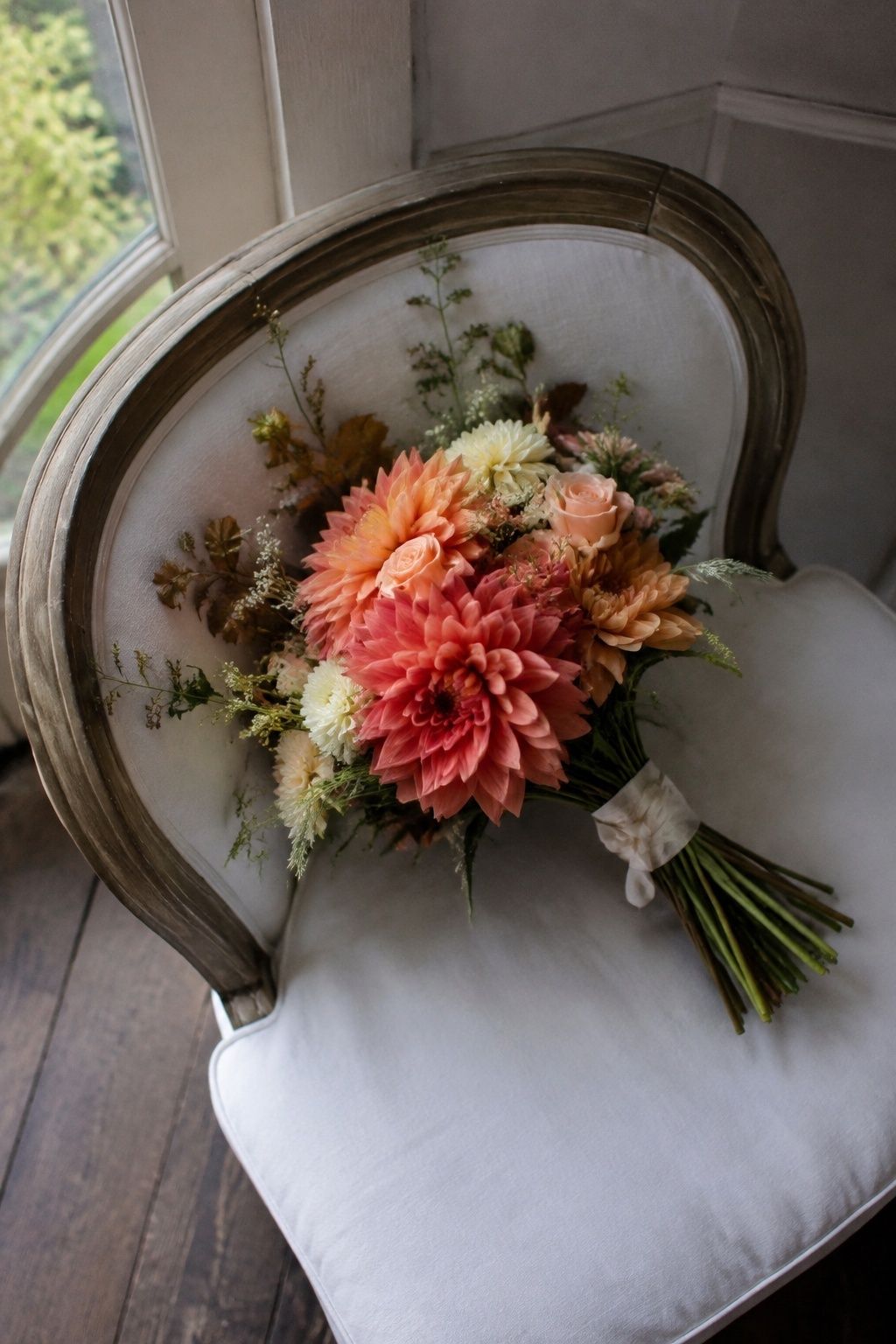 Loose coral and peach dahlia bouquet on a linen chair