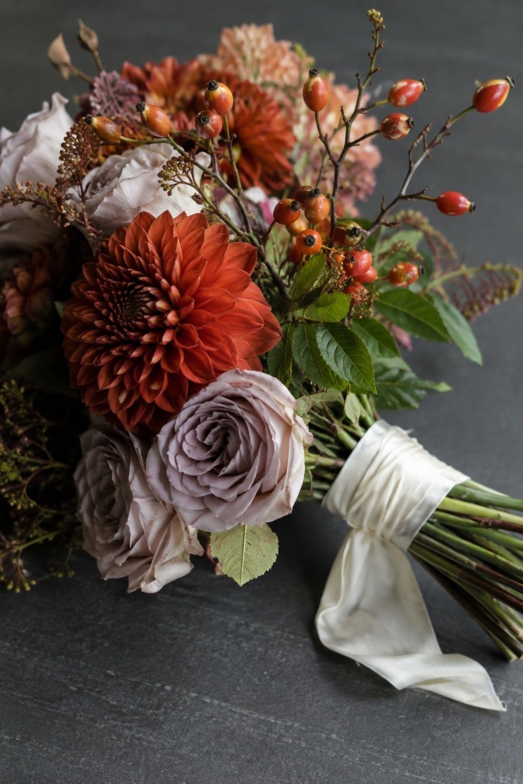 Red rose hips nestled among rust dahlias and mauve roses