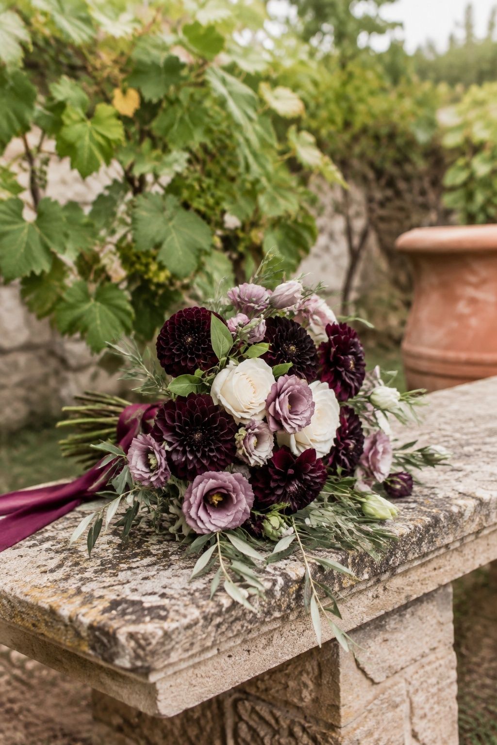 Plum and ivory bridal bouquet with olive foliage on stone