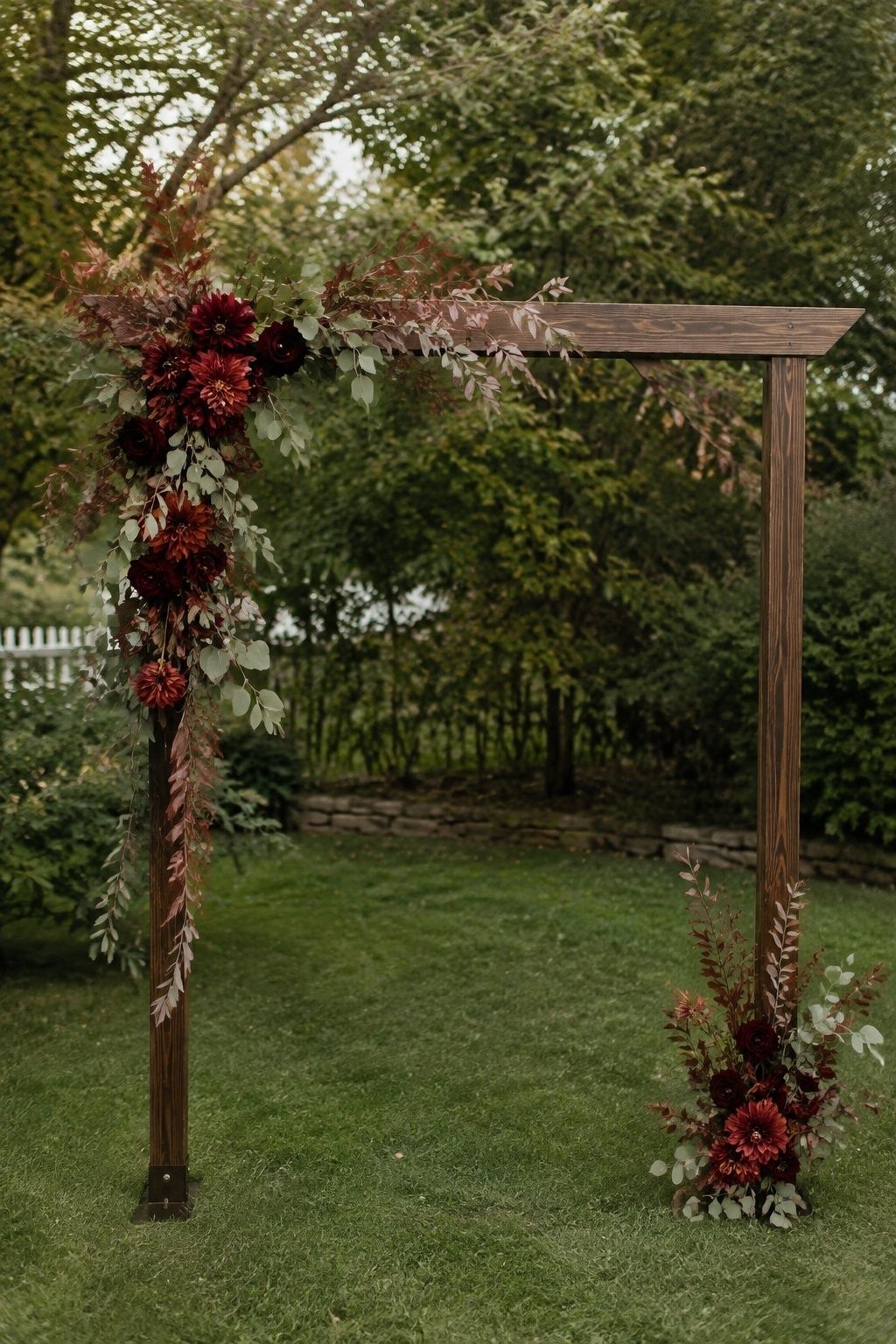 Asymmetrical burgundy and rust florals on a wooden ceremony arch