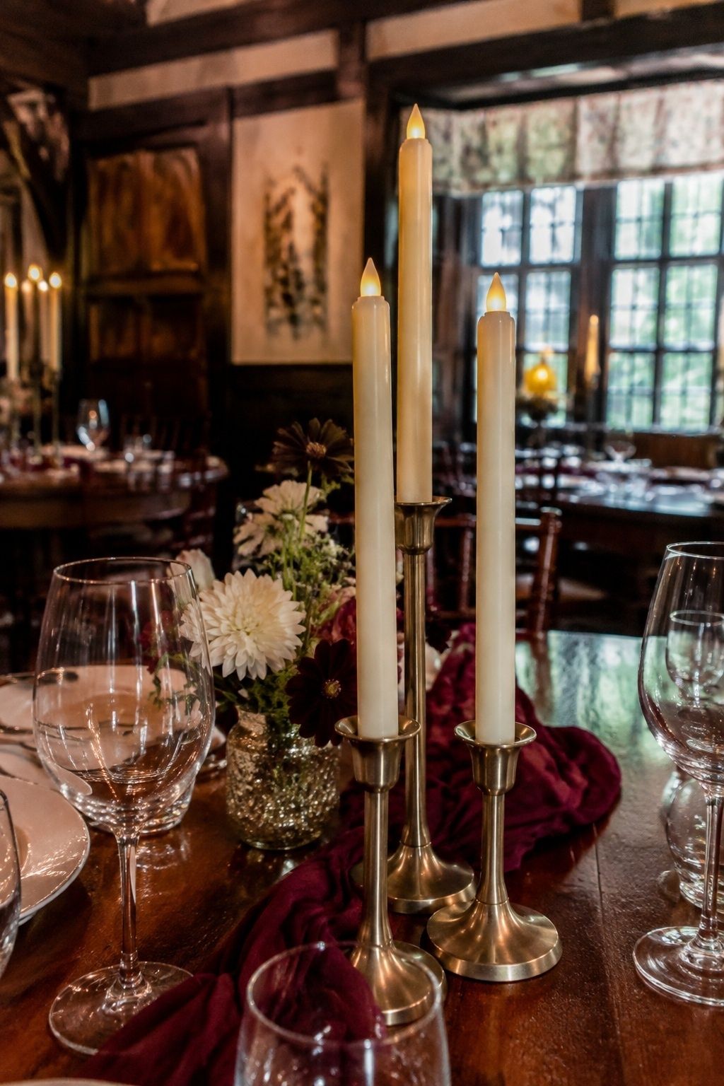 Close three-quarter view of three ivory flameless LED taper candles with visible molded flame tips in brass holders on a historic inn wedding table