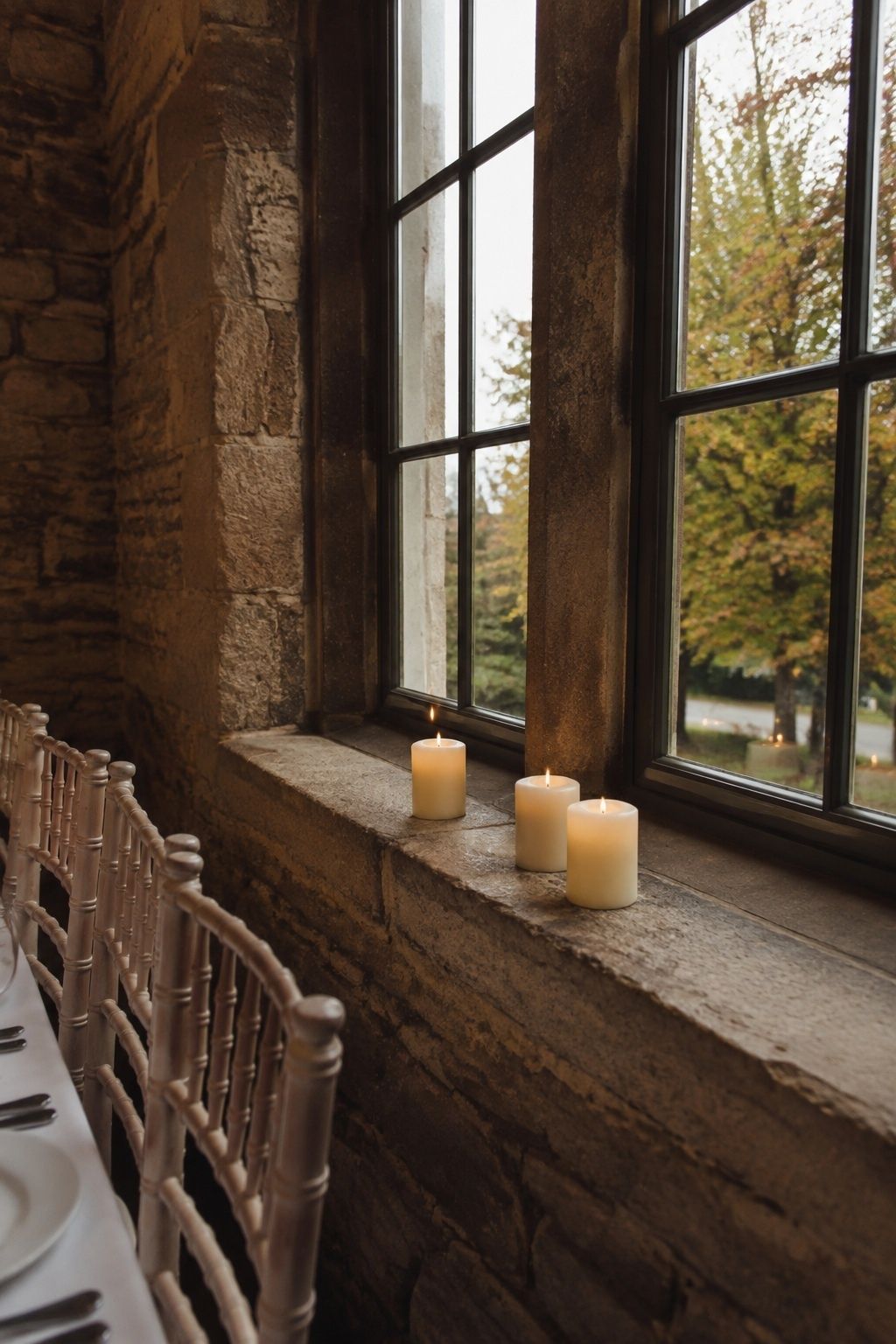 Detail from the side of a broad stone window sill in a country inn wedding room with three low ivory LED pillar candles