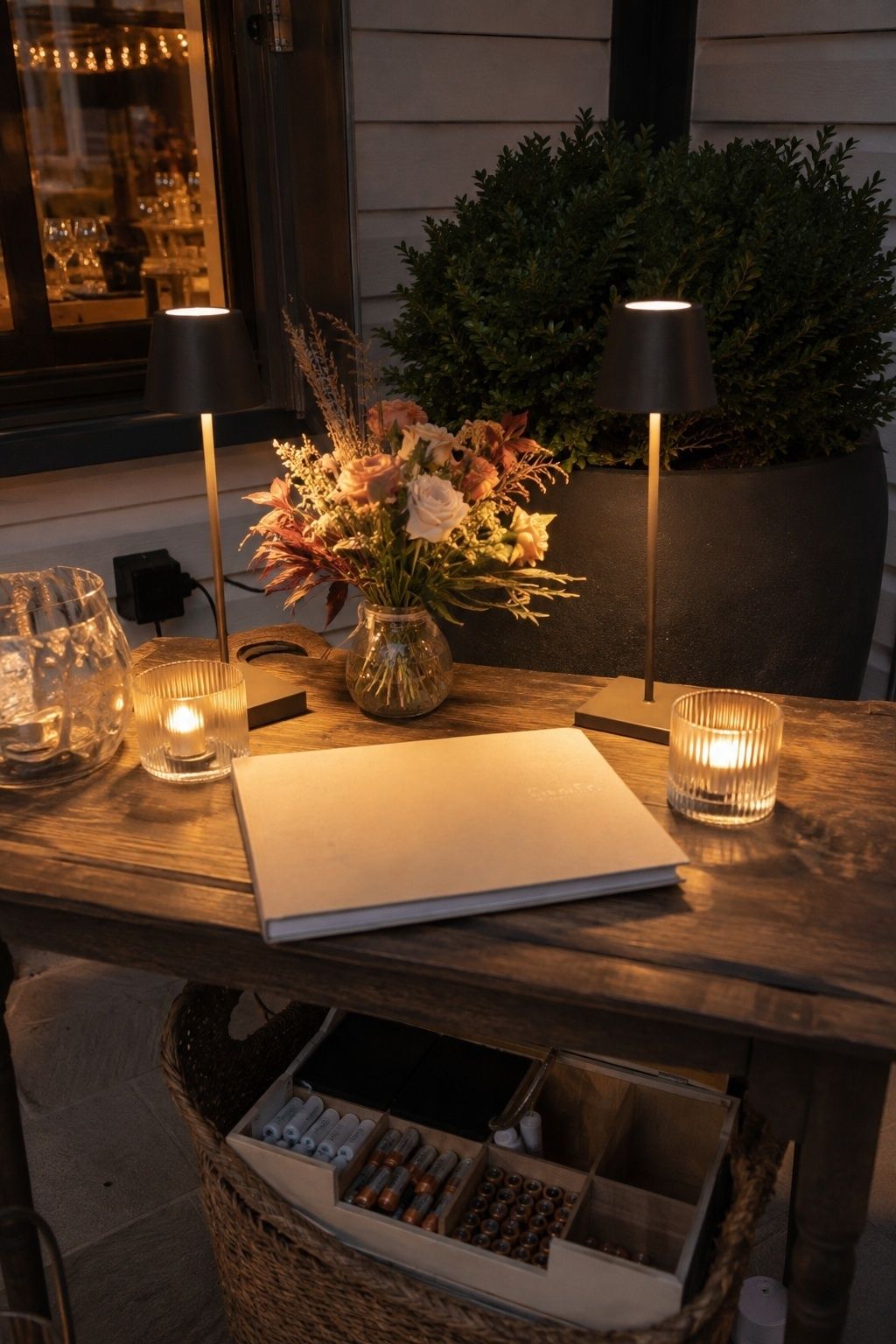 Close oblique photo of a wedding coordinator reserve setup on an outdoor guest-book table at dusk: two charged cordless warm lamps