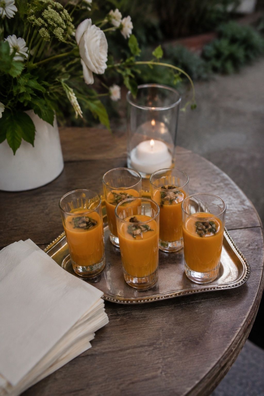 Small tray of six clear narrow shooter glasses filled with smooth orange butternut squash soup, toasted pepitas and chive oil garnish, ivory cocktail napkins, intimate garden wedding cocktail table