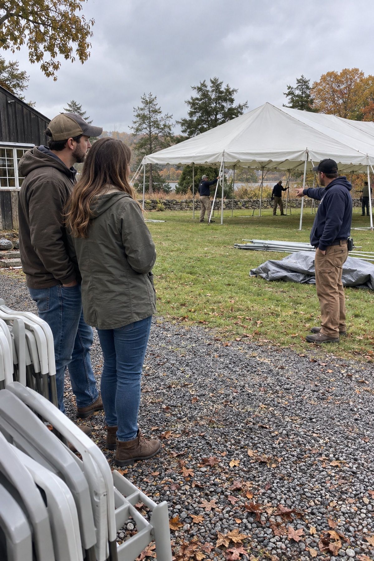 A couple watches a rental crew assemble an ivory tent before their fall wedding.
