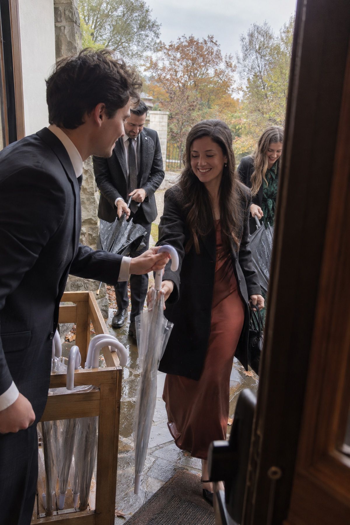 An usher hands a clear umbrella to an arriving fall wedding guest at the entrance.