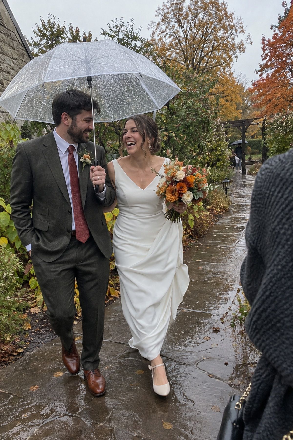 A newlywed couple shares a candid rainy portrait beneath a clear umbrella.