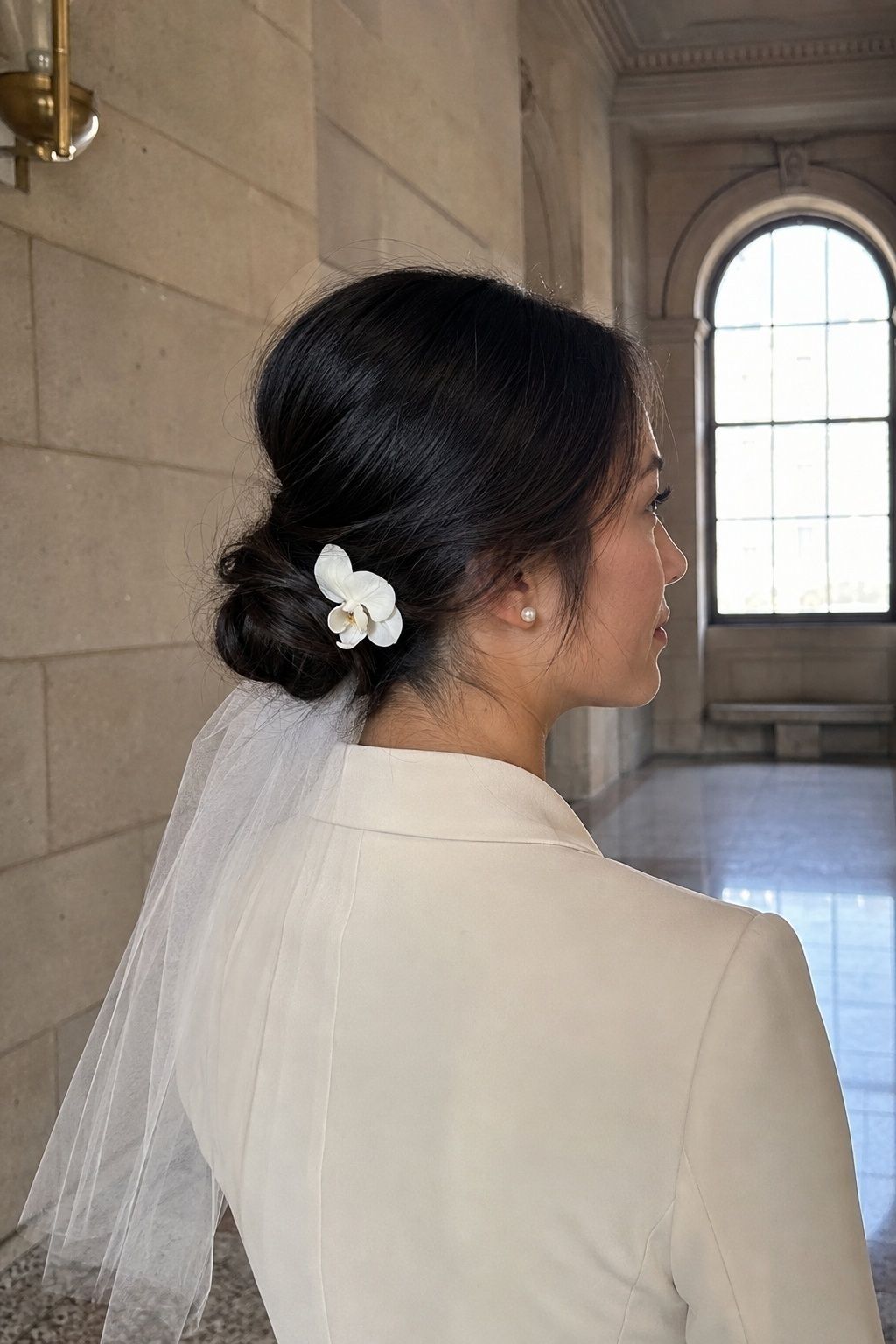 Courthouse bride in an ivory suit with a petite low bun, short veil, and one white orchid