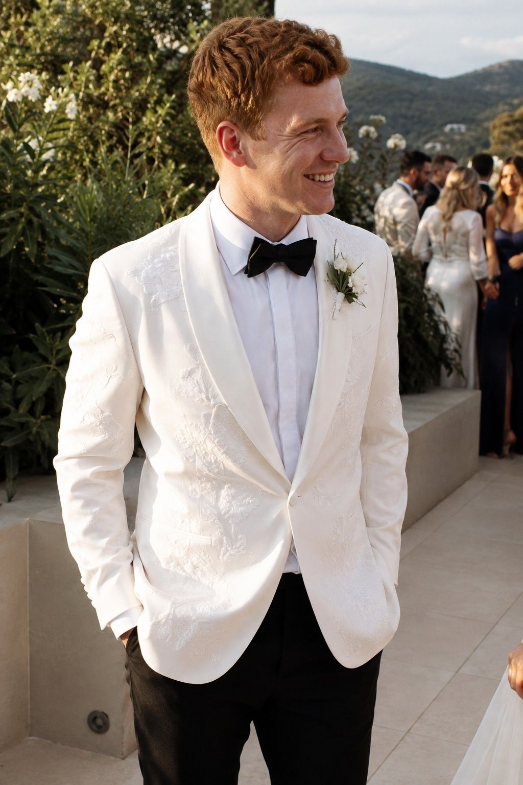 White floral embroidered blazer with a black bow tie and trousers.